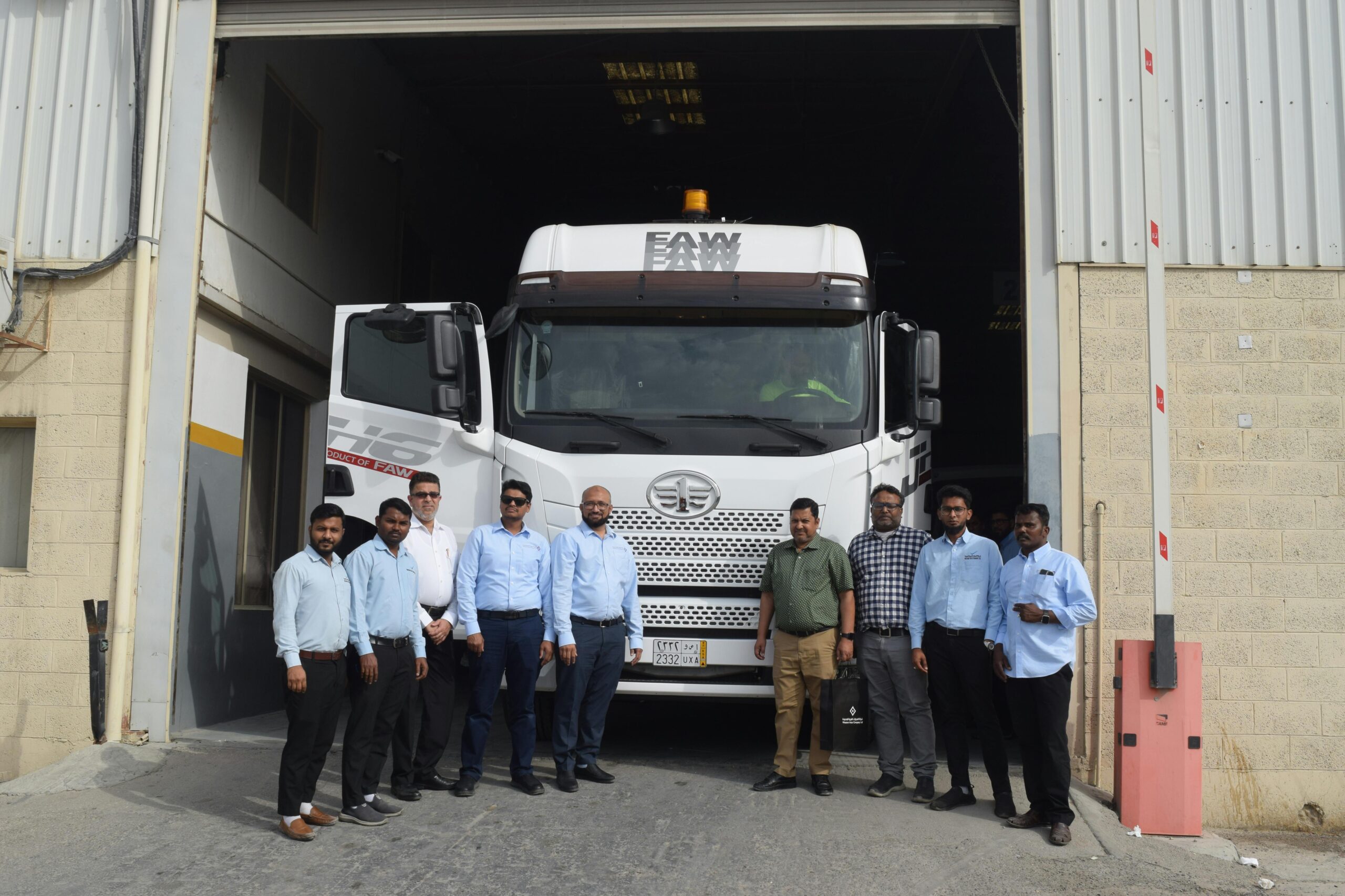Eine Gruppe von Menschen steht vor einem FAW-Truck, der am Eingang eines Lagerhauses geparkt ist, und demonstriert Teamwork.