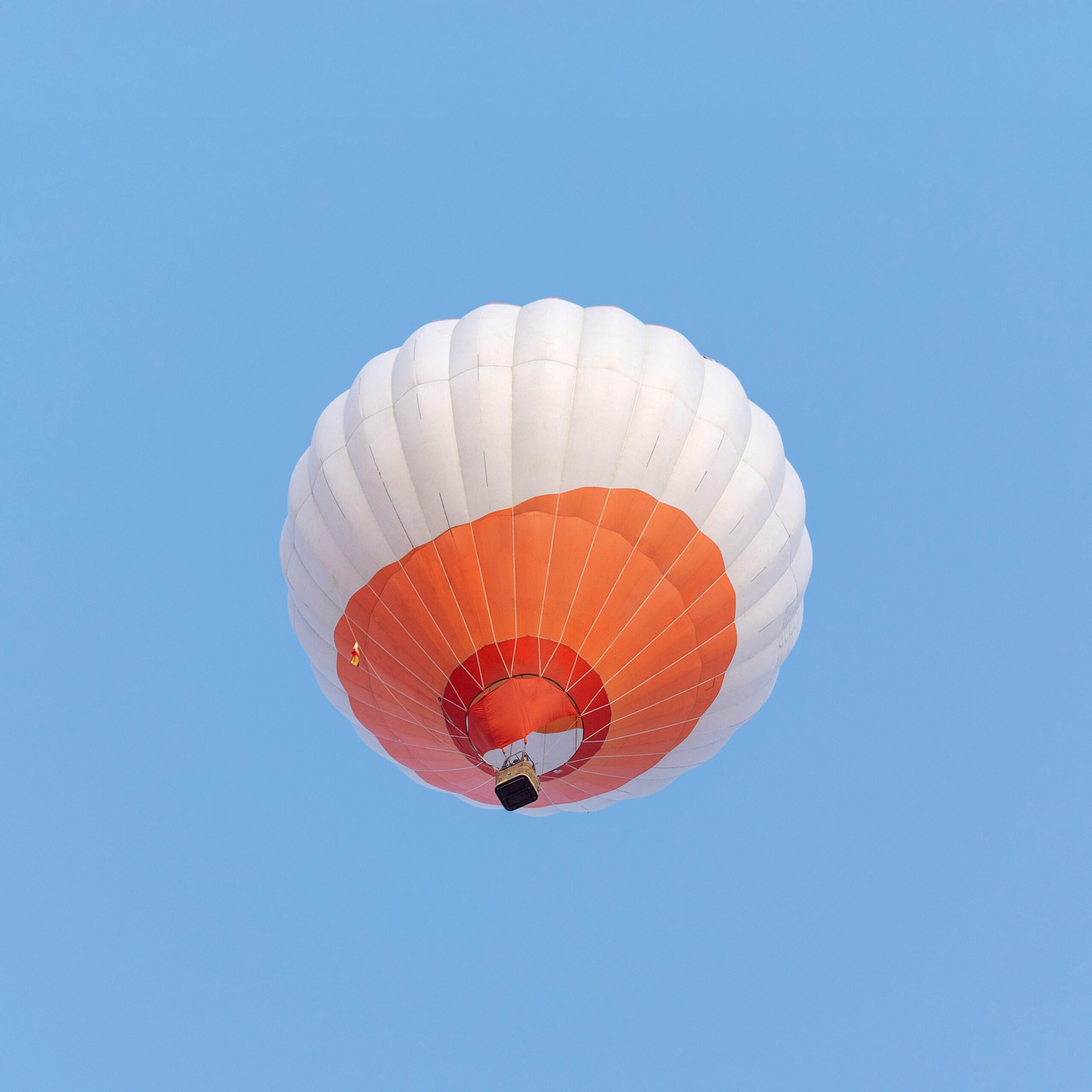 Ein leuchtend orange-weißer Heißluftballon schwebt vor einem klaren blauen Himmel in Valladolid, Spanien.
