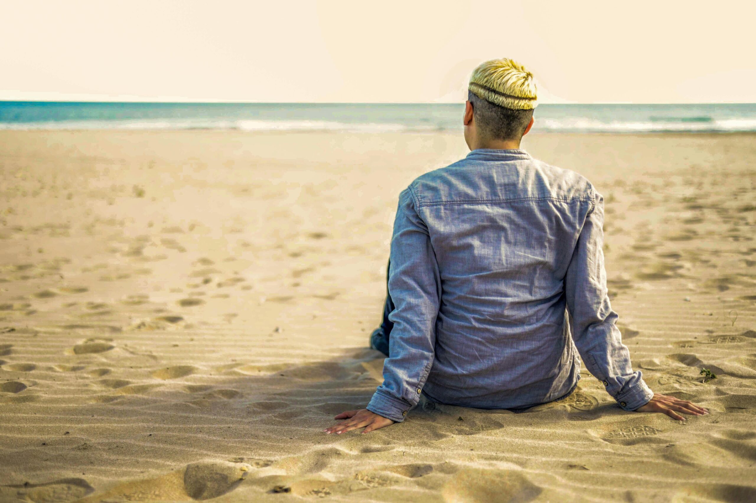 Person, die allein an einem sonnigen Strand sitzt und einen ruhigen Moment am Meer genießt.