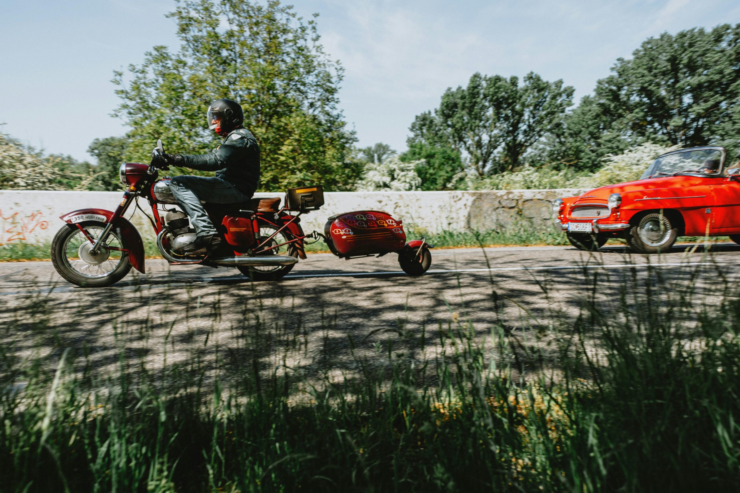 Ein Oldtimer-Motorrad mit Beiwagen überholt auf einer sonnigen Landstraße einen Oldtimer und weckt Nostalgie.