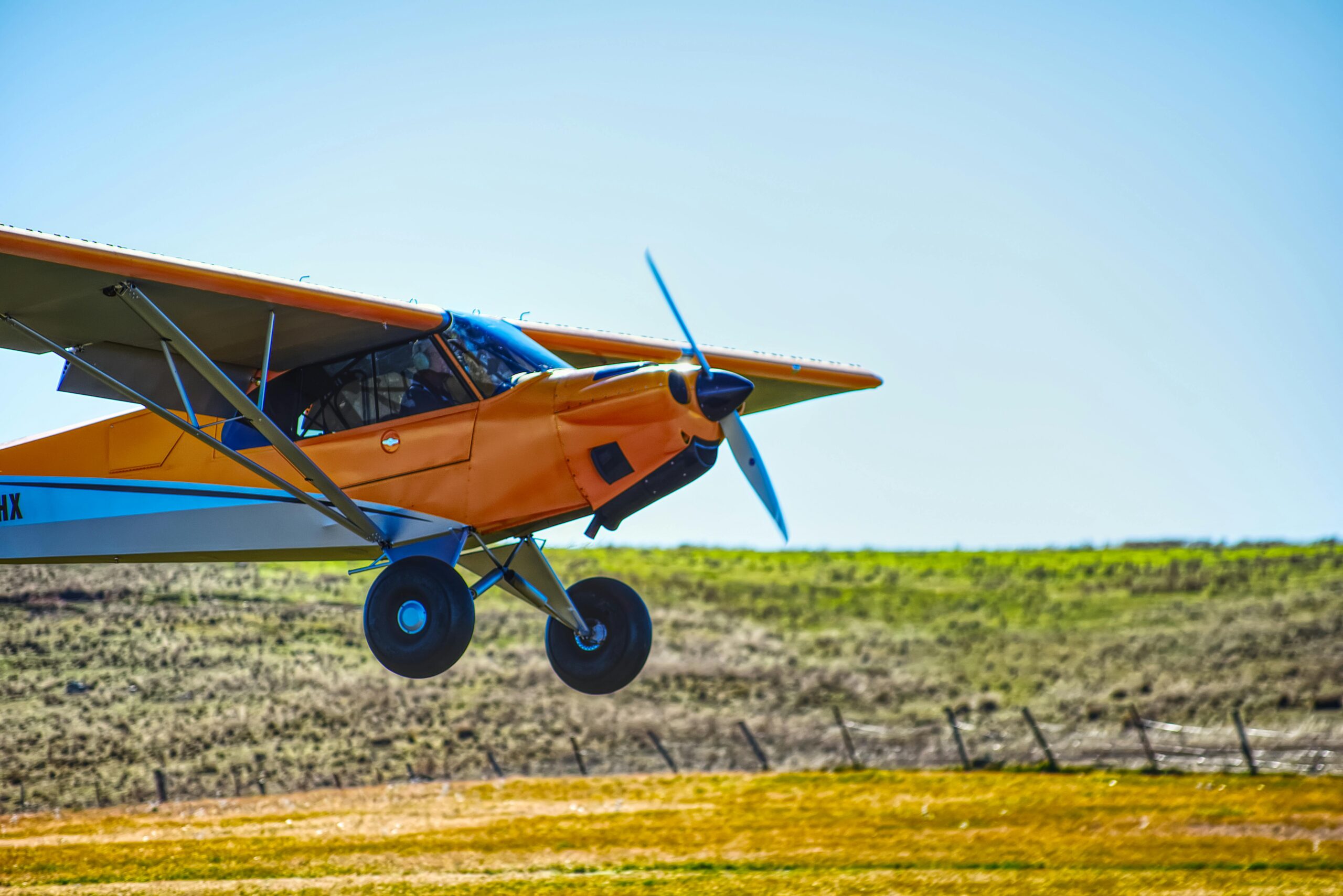 An einem hellen, klaren Tag schwebt ein orangefarbenes Flugzeug über der Landschaft.