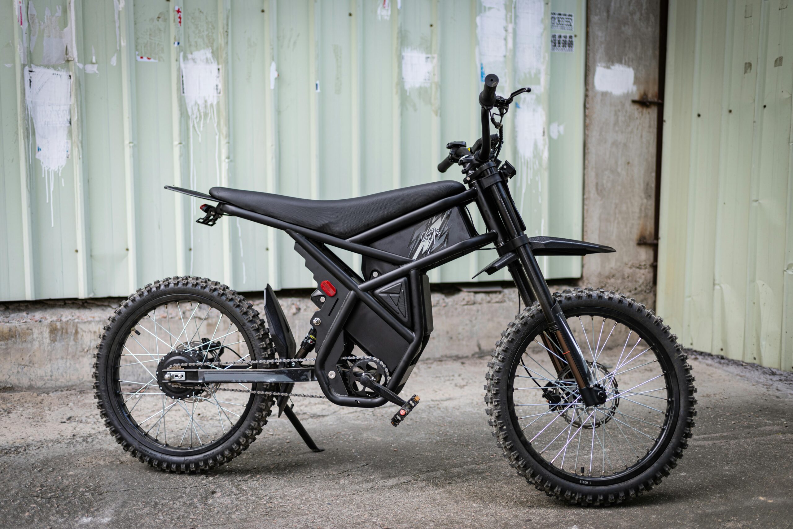Vor einer Wellblechwand steht ein modernes schwarzes Elektrofahrrad mit robusten Reifen.