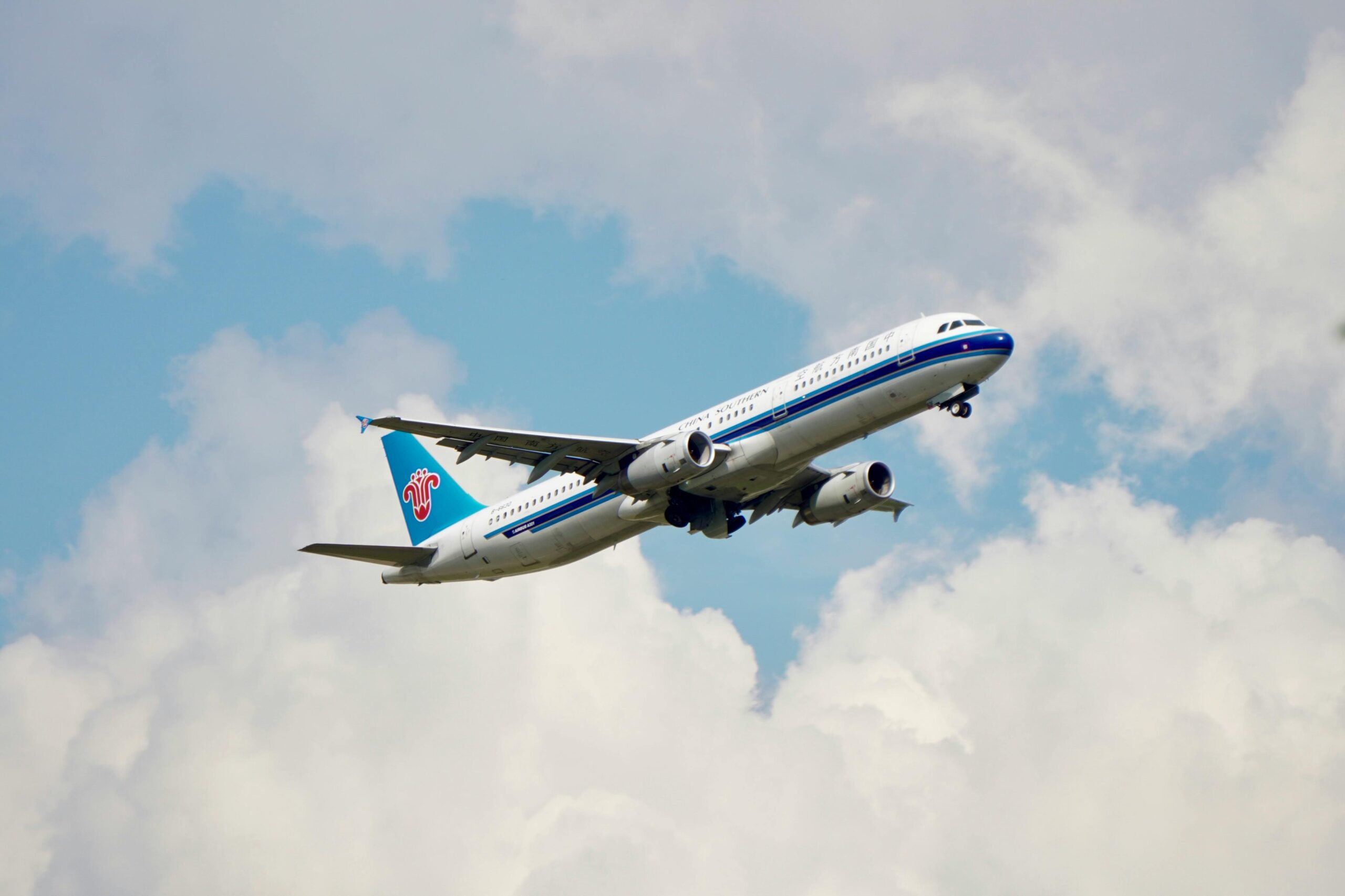 Ein Verkehrsflugzeug fliegt vor dem Hintergrund eines blauen Himmels mit Wolken und symbolisiert Reisen und Freiheit.
