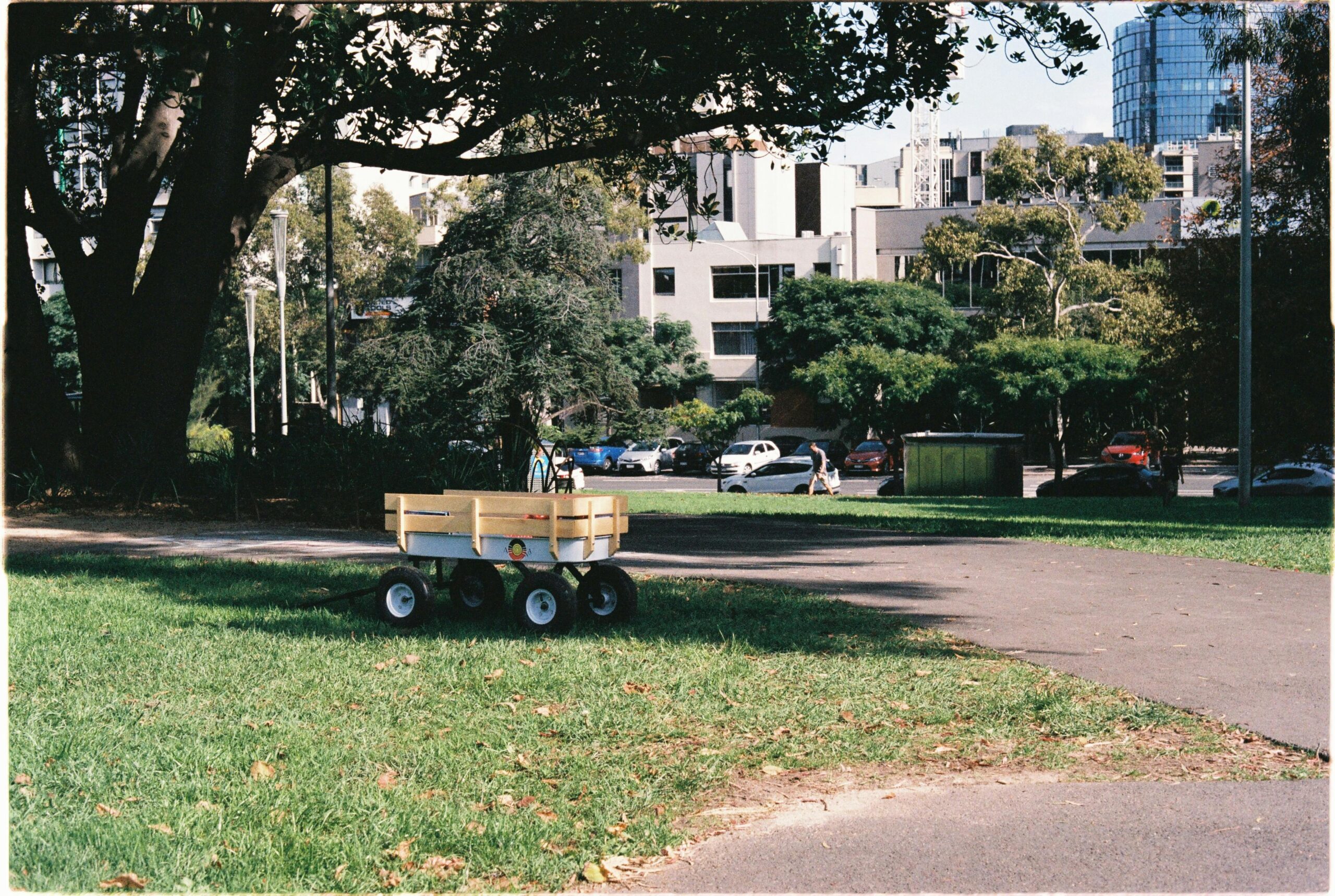 Ein einsamer gelber Wagen steht auf üppigem grünem Gras in einem Park in Melbourne, im Hintergrund sind Stadtgebäude zu sehen.