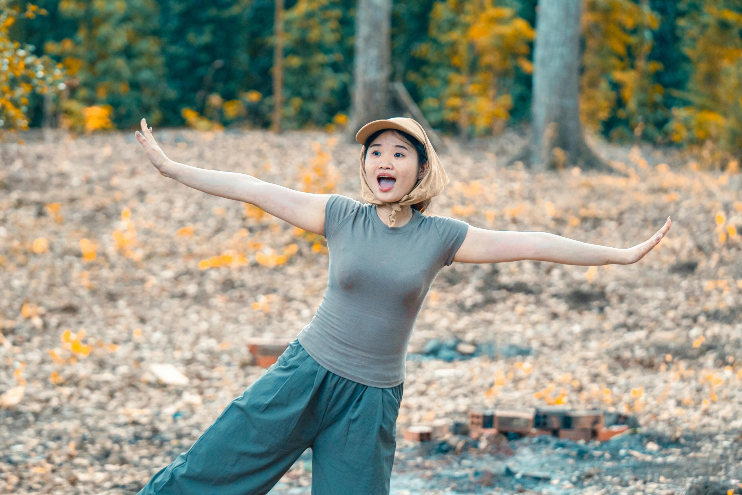 Eine glückliche Frau posiert spielerisch in einem herbstlichen Wald und drückt ihre Freude aus.