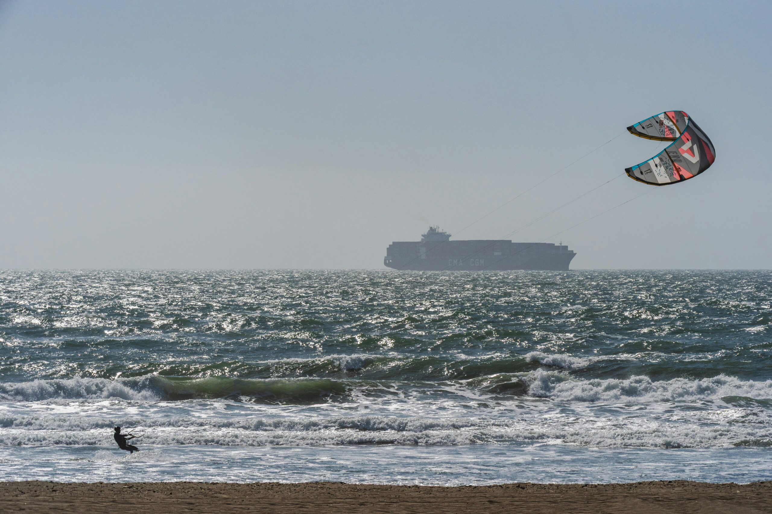 Dynamische Szene des Kitesurfens in der Nähe eines Frachtschiffs auf offener See.