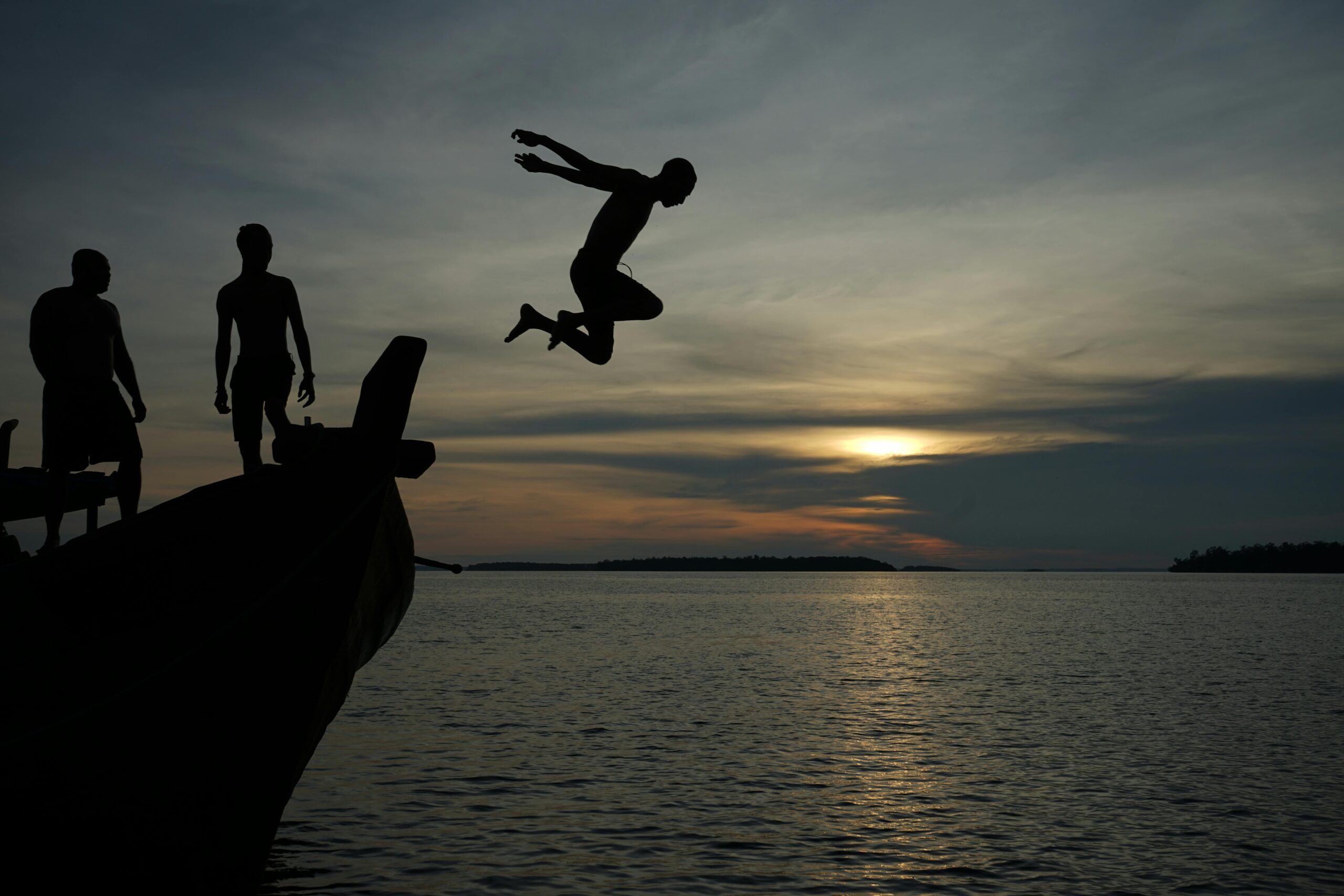 Silhouetten von Figuren, die bei Sonnenuntergang in der Nähe von Sorong, Indonesien, von einem Boot ins Meer springen.