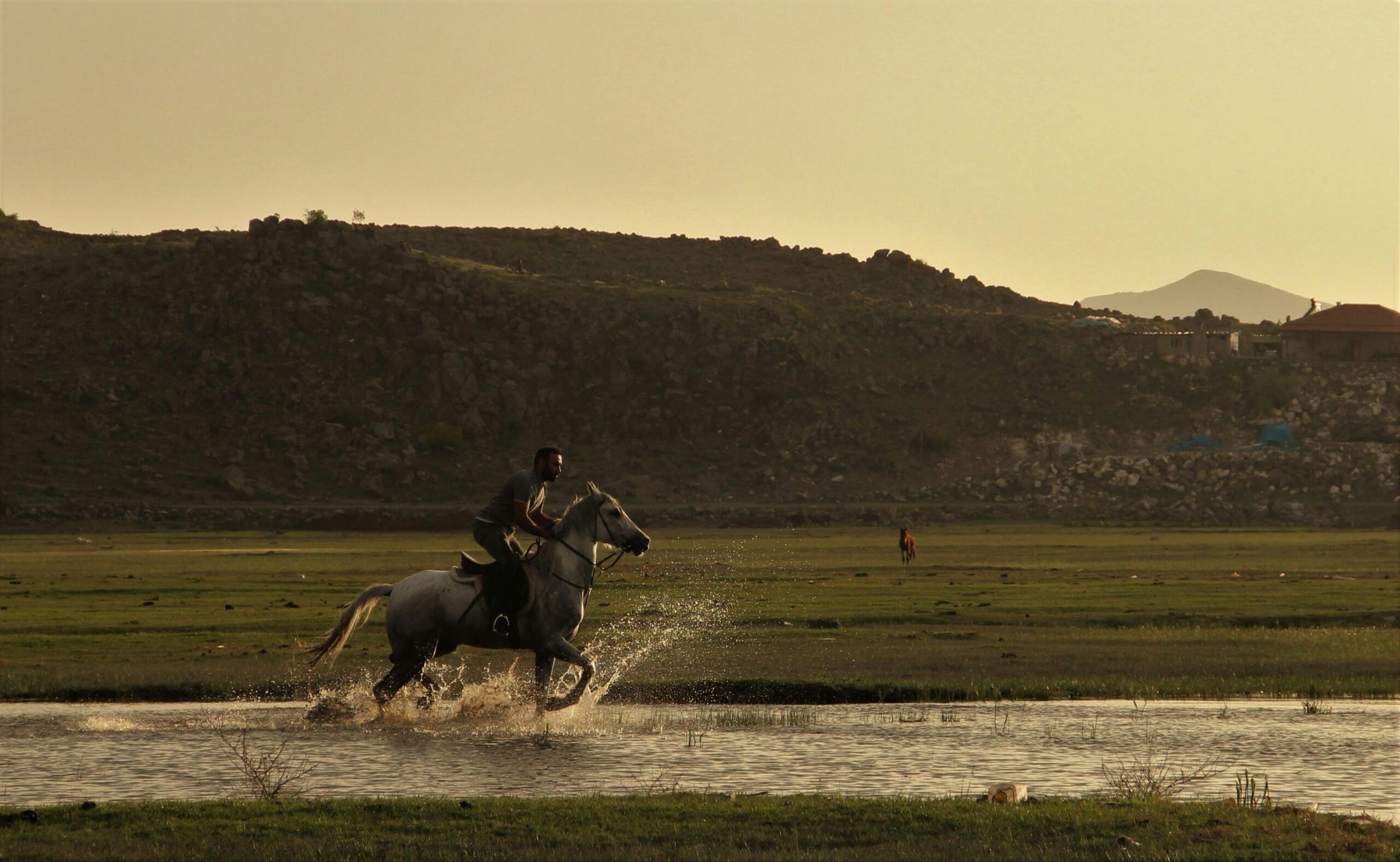 Ein Reiter galoppiert vor einer Bergkulisse in Kayseri, Türkei, durchs Wasser.