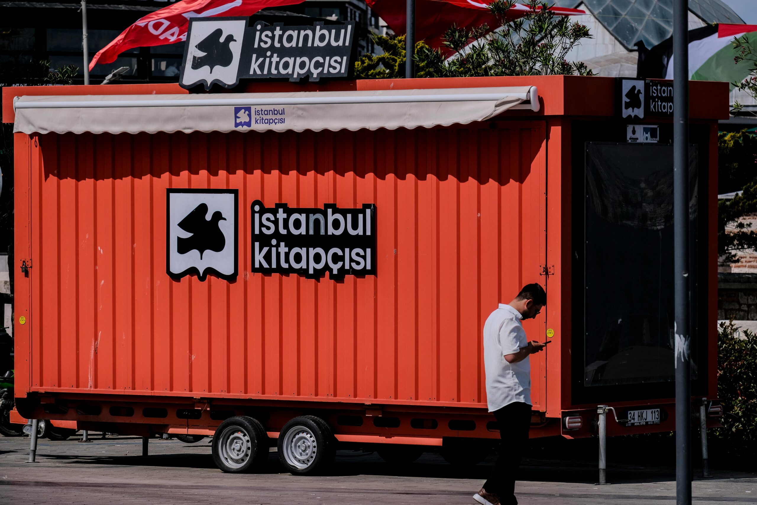 Leuchtend roter Containerbuchladen auf der Straße von Istanbul mit einem Passanten, der ein Smartphone benutzt.
