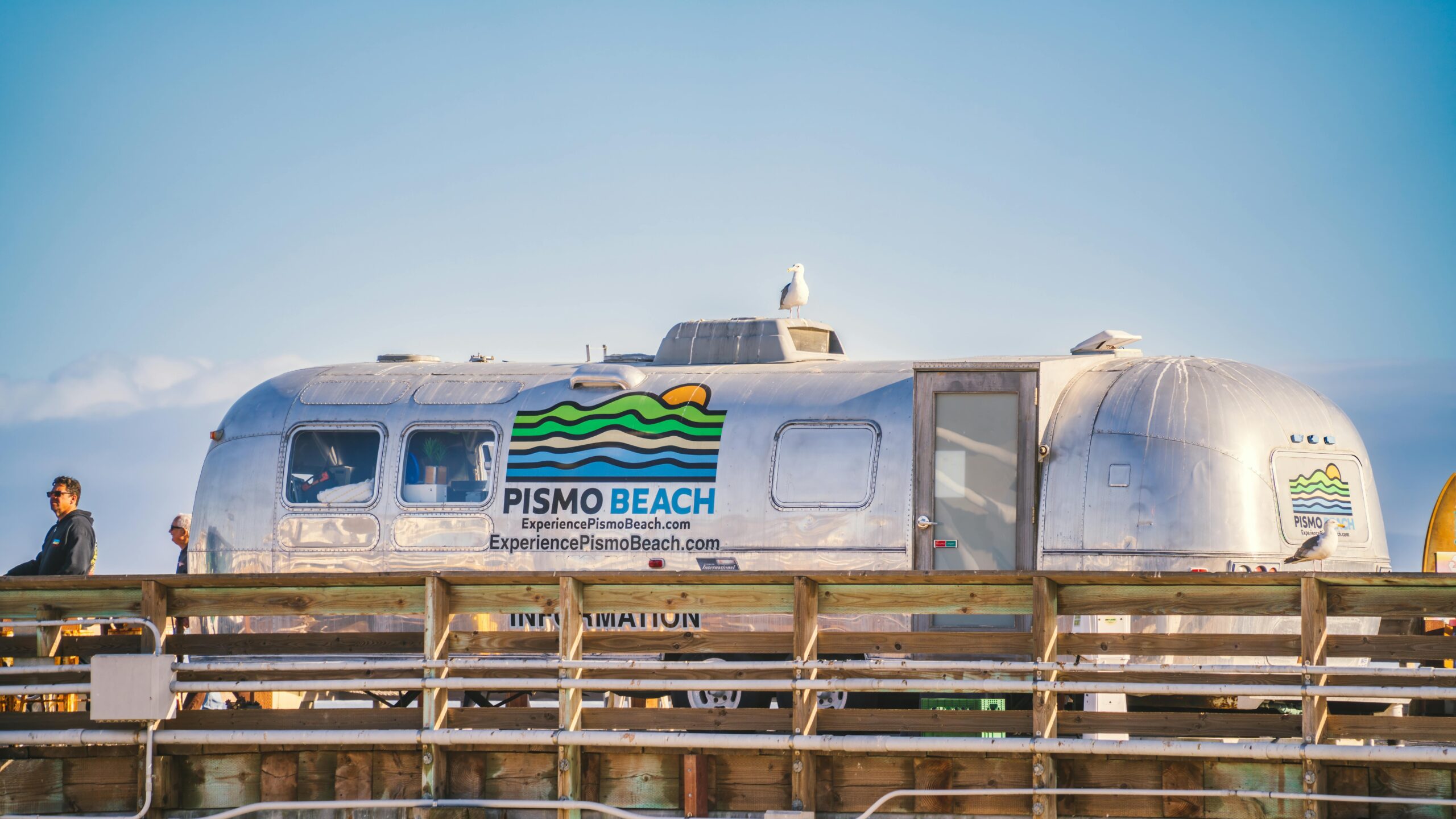 Informationsanhänger am Pismo Beach Pier unter einem klaren blauen Himmel.