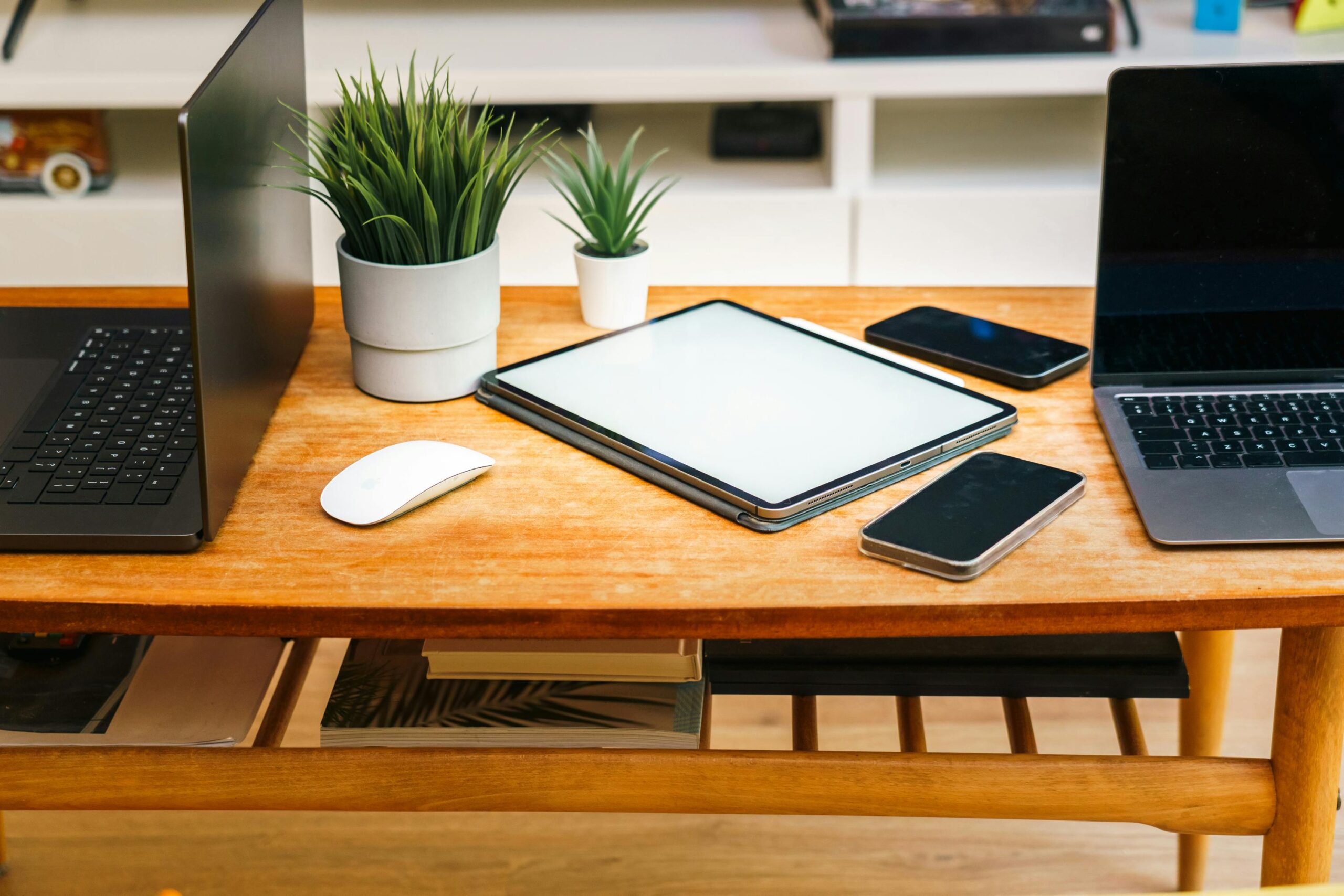 Ein stilvoller Home-Office-Schreibtisch mit Laptops, Tablet, Smartphones und Topfpflanzen.