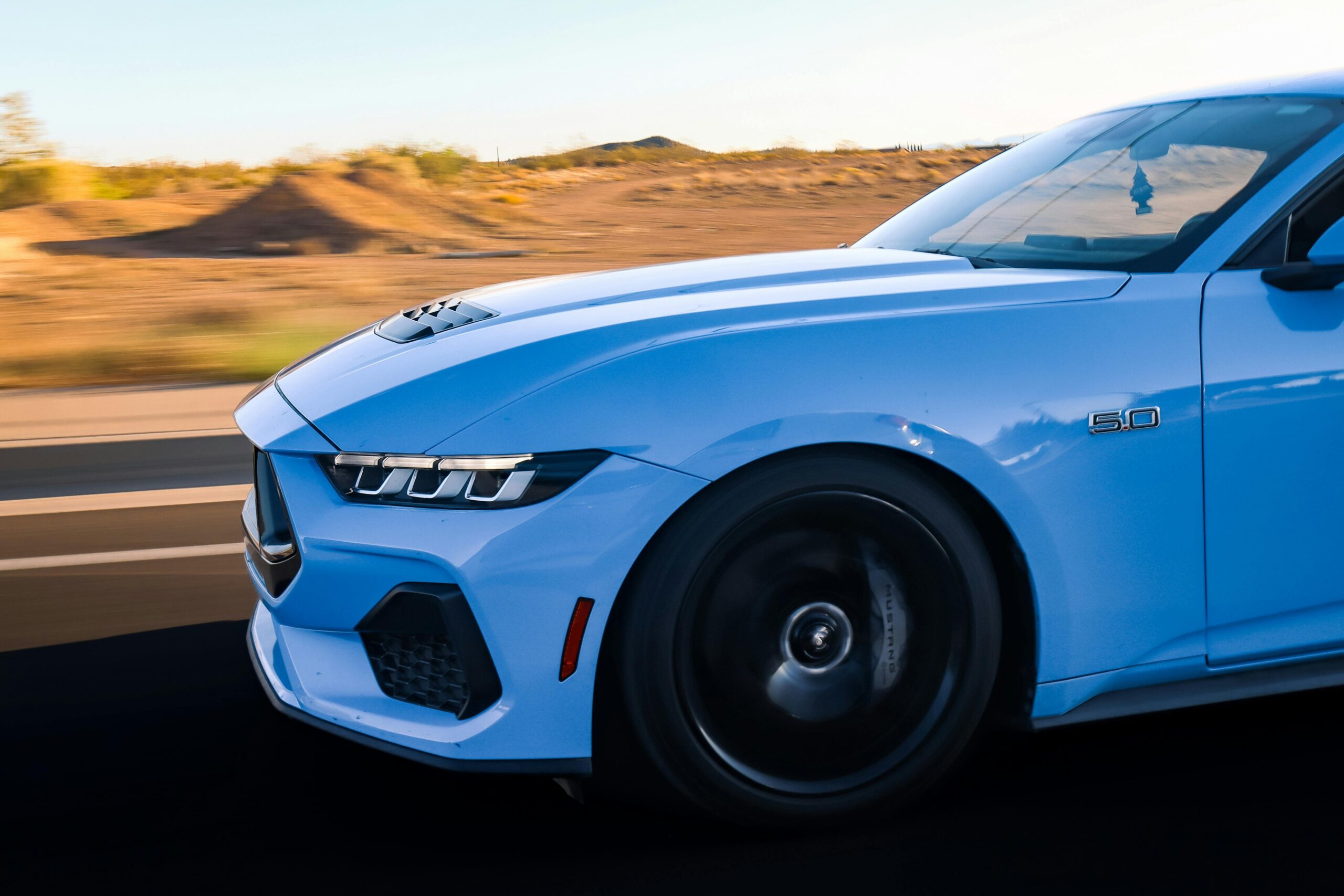 Dynamische Aufnahme eines blauen Sportwagens, der bei Sonnenuntergang schnell auf einer Autobahn fährt.