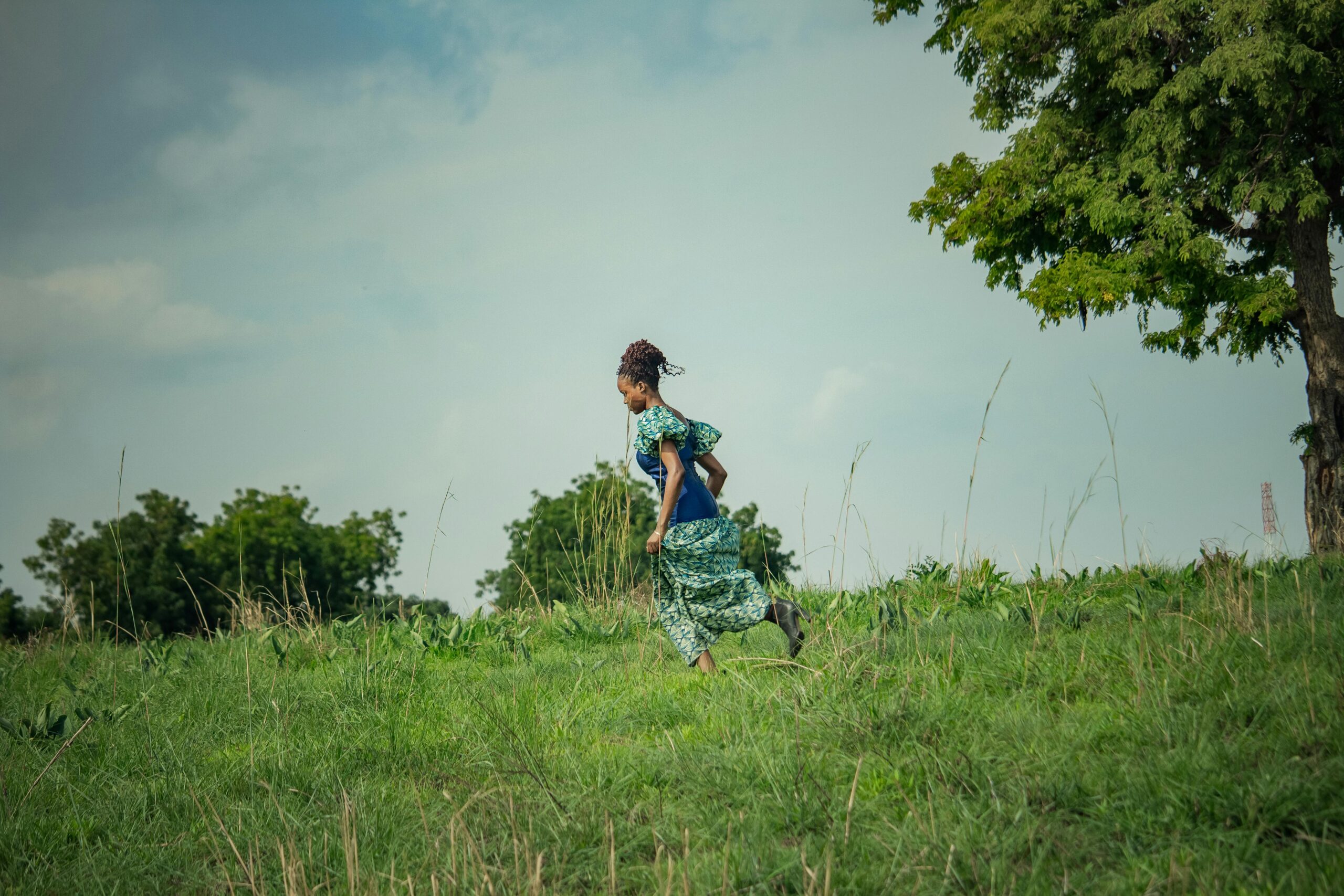 Eine Frau im Kleid läuft unter blauem Himmel durch eine sonnige Wiese.