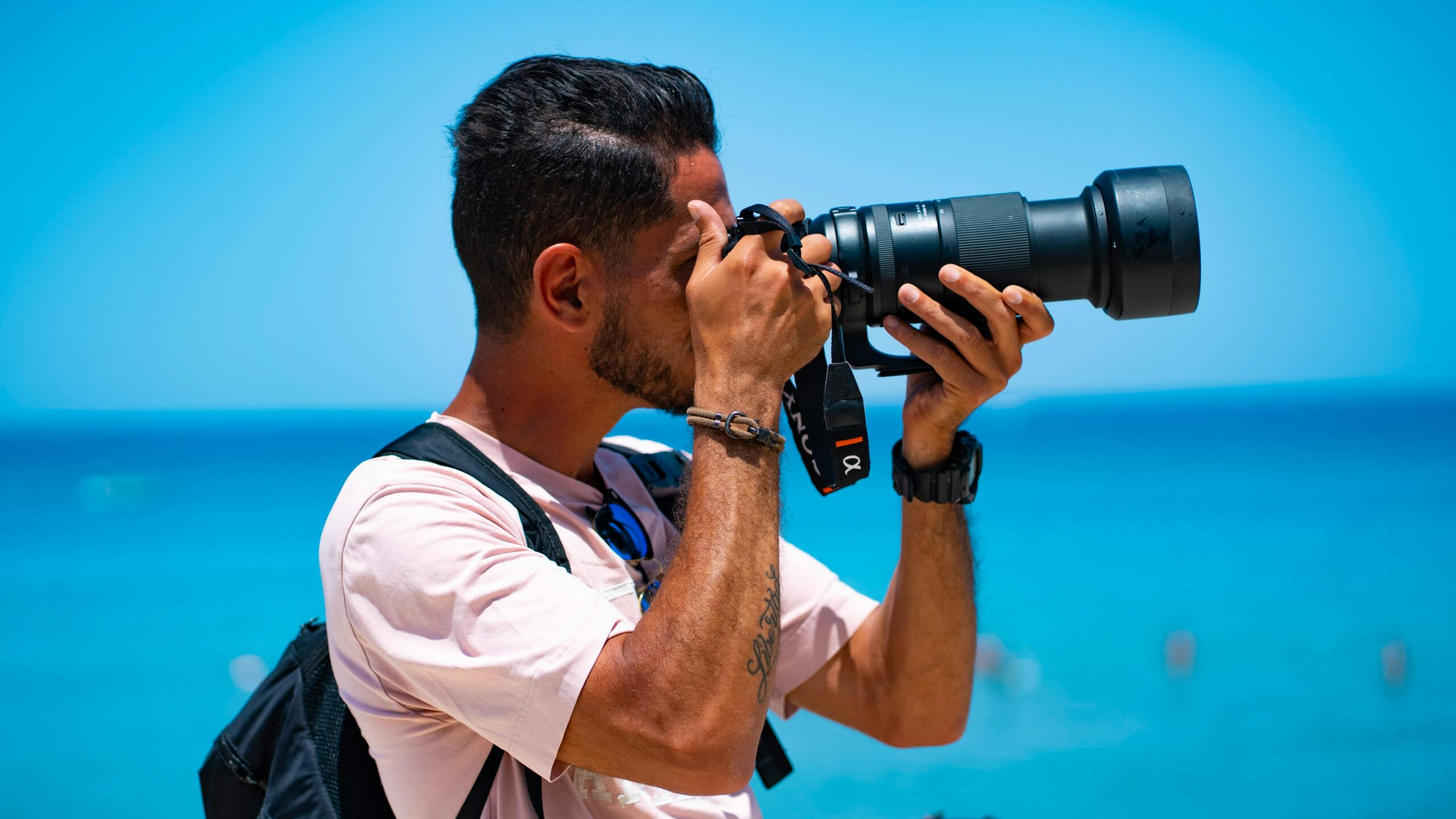 Fotograf mit Kamera an einem hellen Strand in Sizilien, Italien, und genießt die sommerliche Aussicht auf das Meer.
