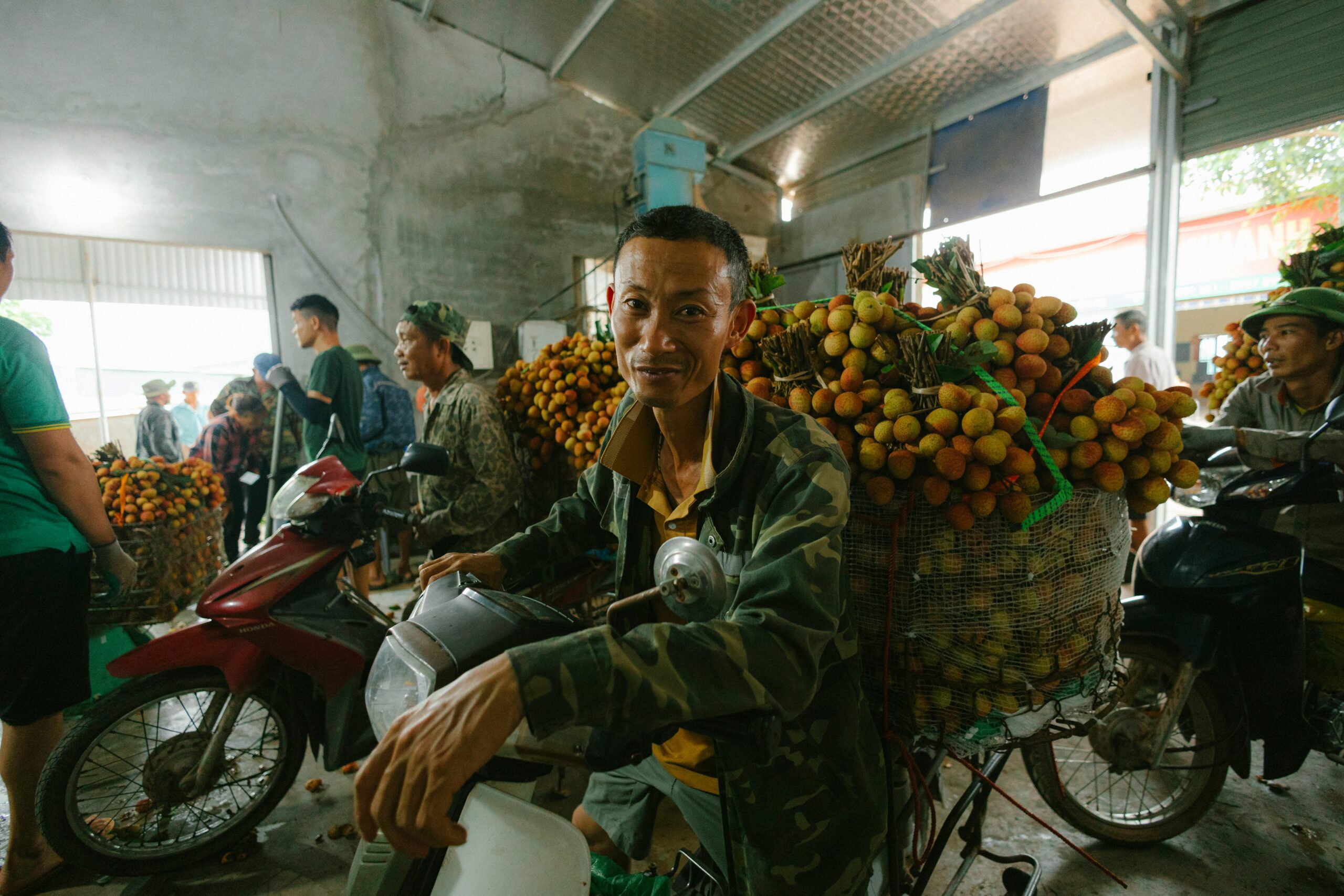 Eine geschäftige Markthalle mit Litschiverkäufern und Motorrädern voller frischem Obst, die den lokalen Handel ankurbeln.