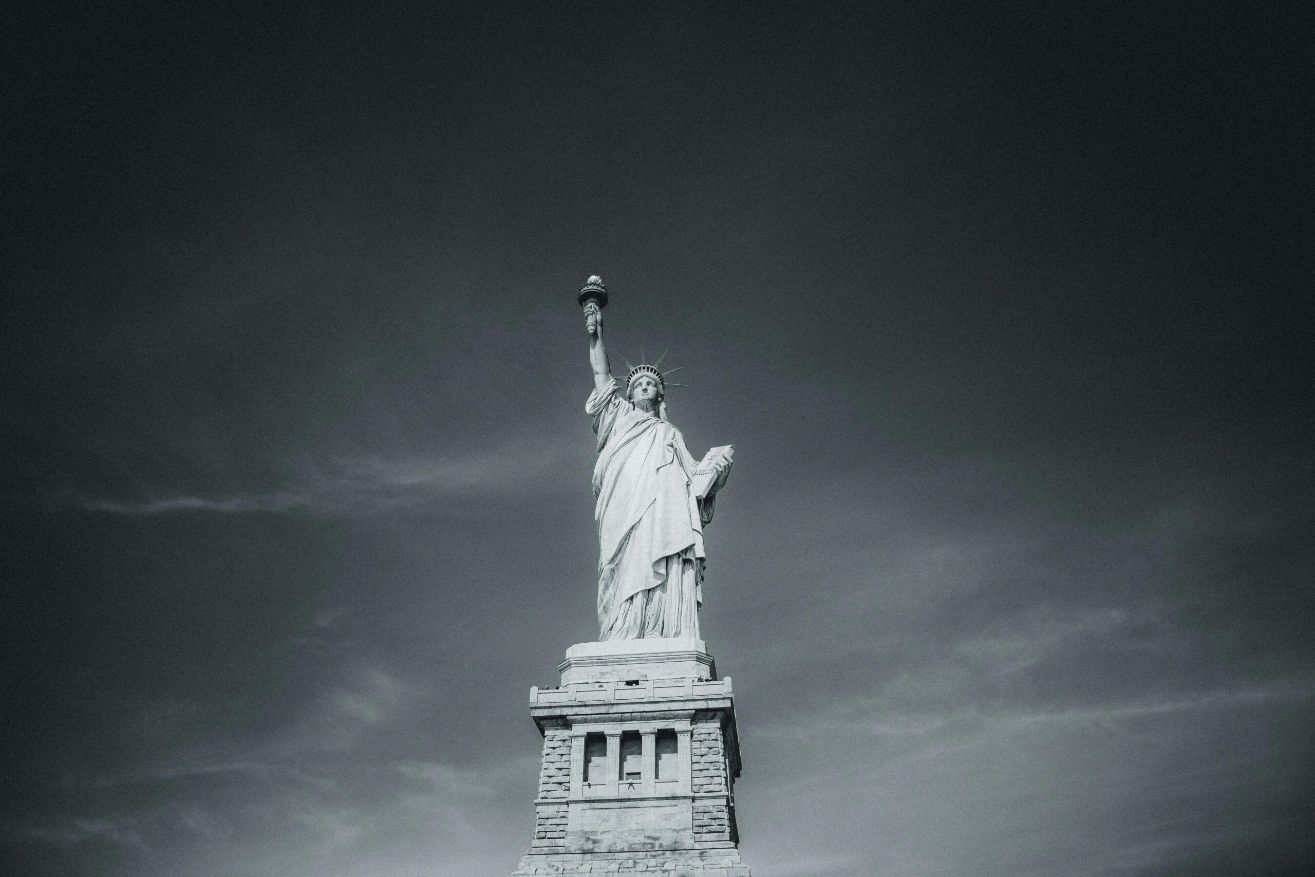 Schwarzweißfoto der Freiheitsstatue, die hoch in den Himmel über New York City ragt.