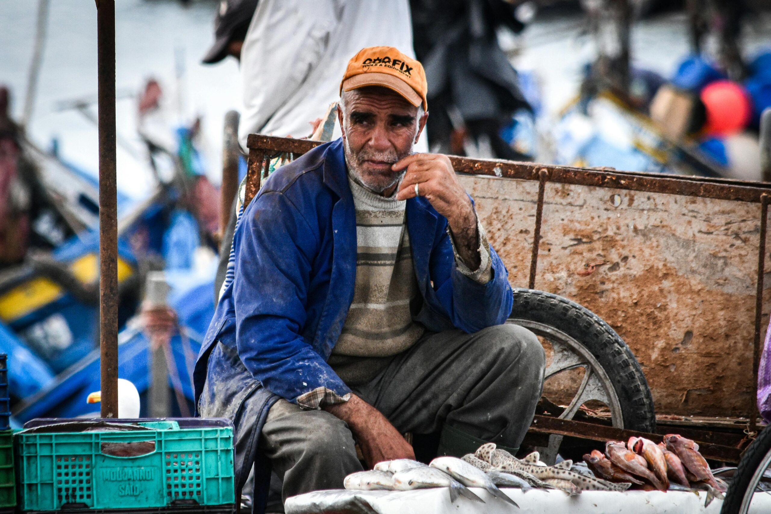 Ein älterer Fischer sitzt am geschäftigen Dock eines Fischmarkts.