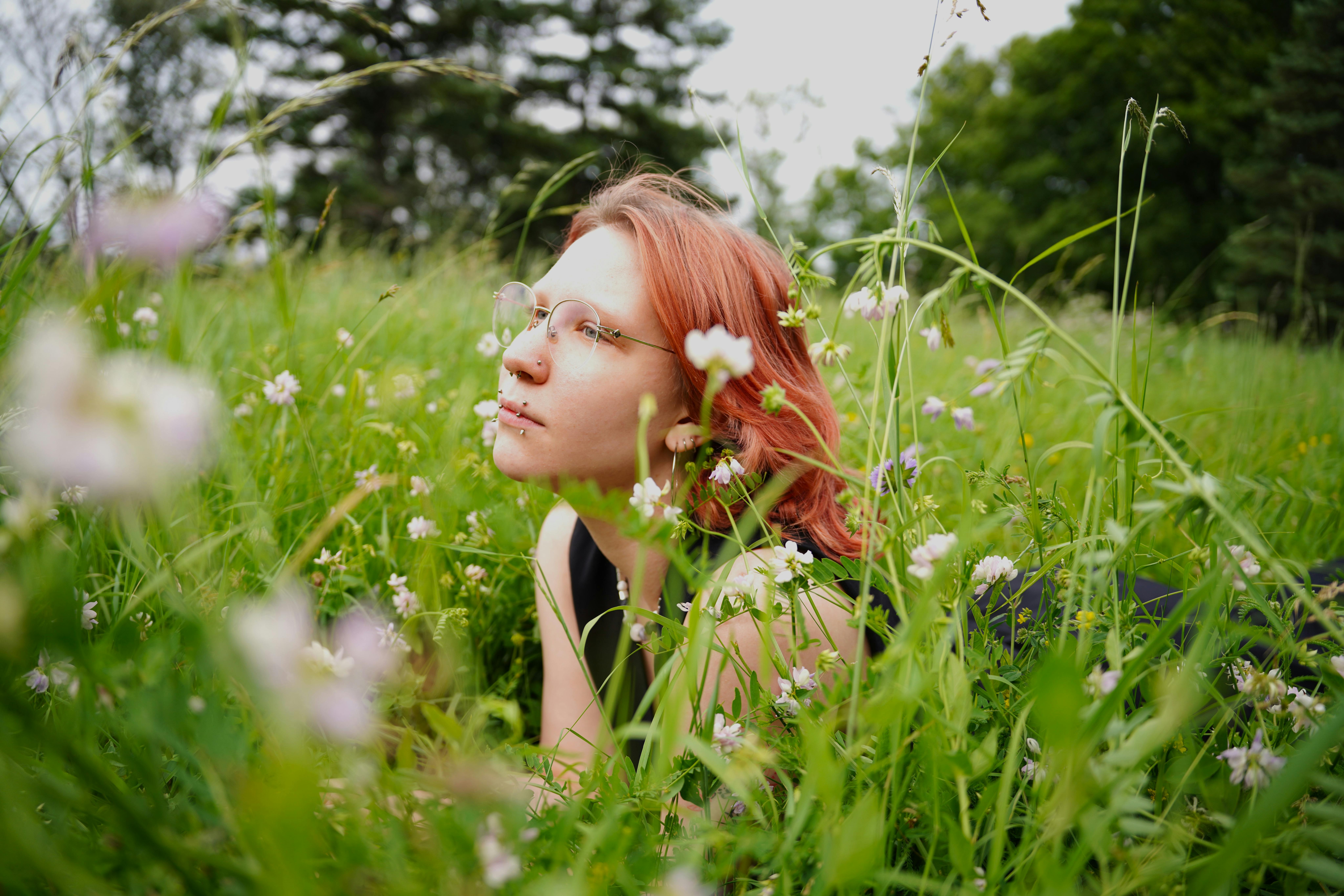 Rothaarige Frau liegt auf einer leuchtend grünen Wiese, umgeben von Wildblumen, und genießt einen ruhigen Tag.