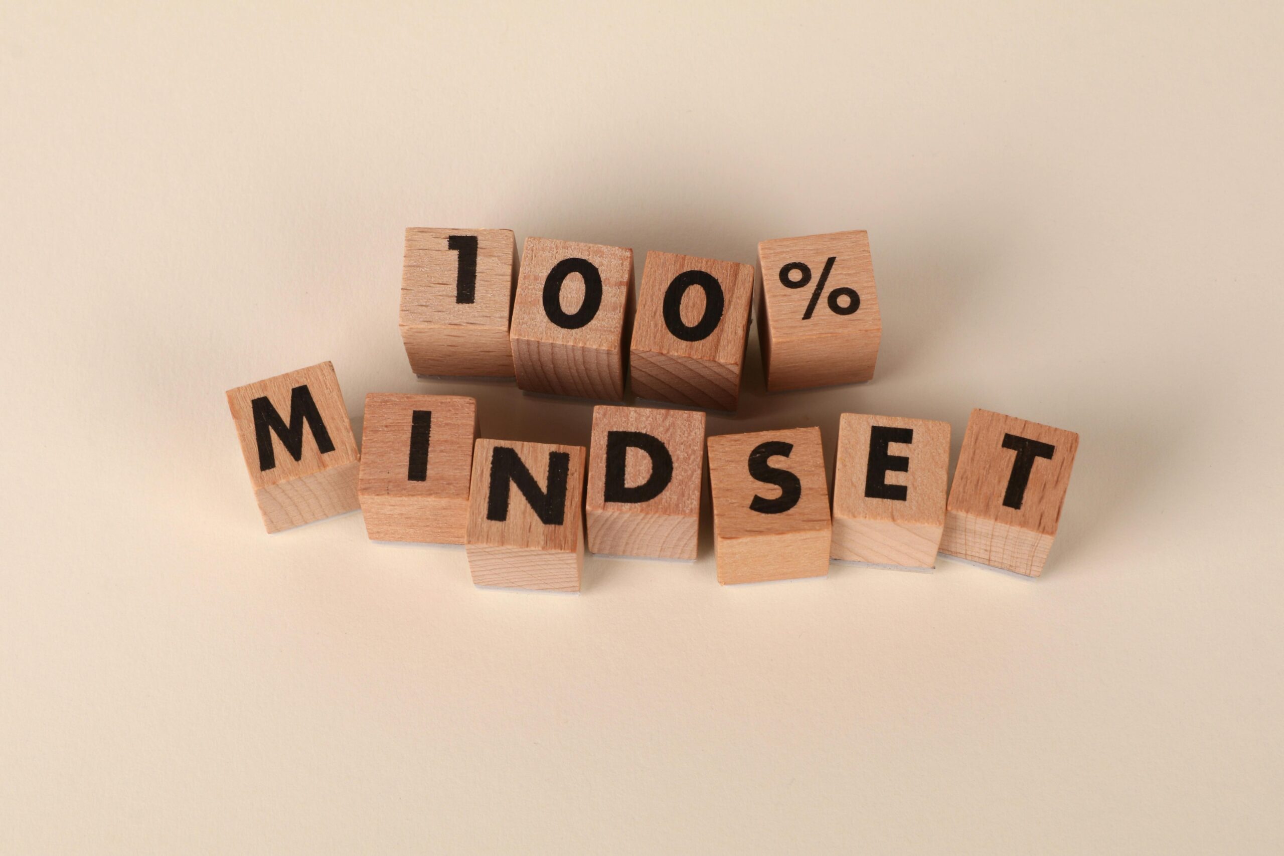 Auf einem neutralen beigen Hintergrund sind Holzklötze so angeordnet, dass sie das Wort „100 % Mindset“ buchstabieren und so Positivität fördern.