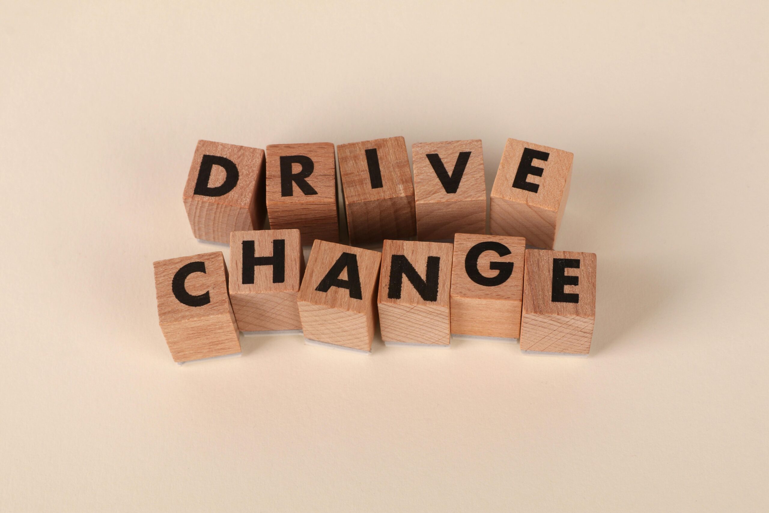 Holzklötze mit der Aufschrift „Drive Change“ auf neutralem Hintergrund symbolisieren Motivation und Wachstum.
