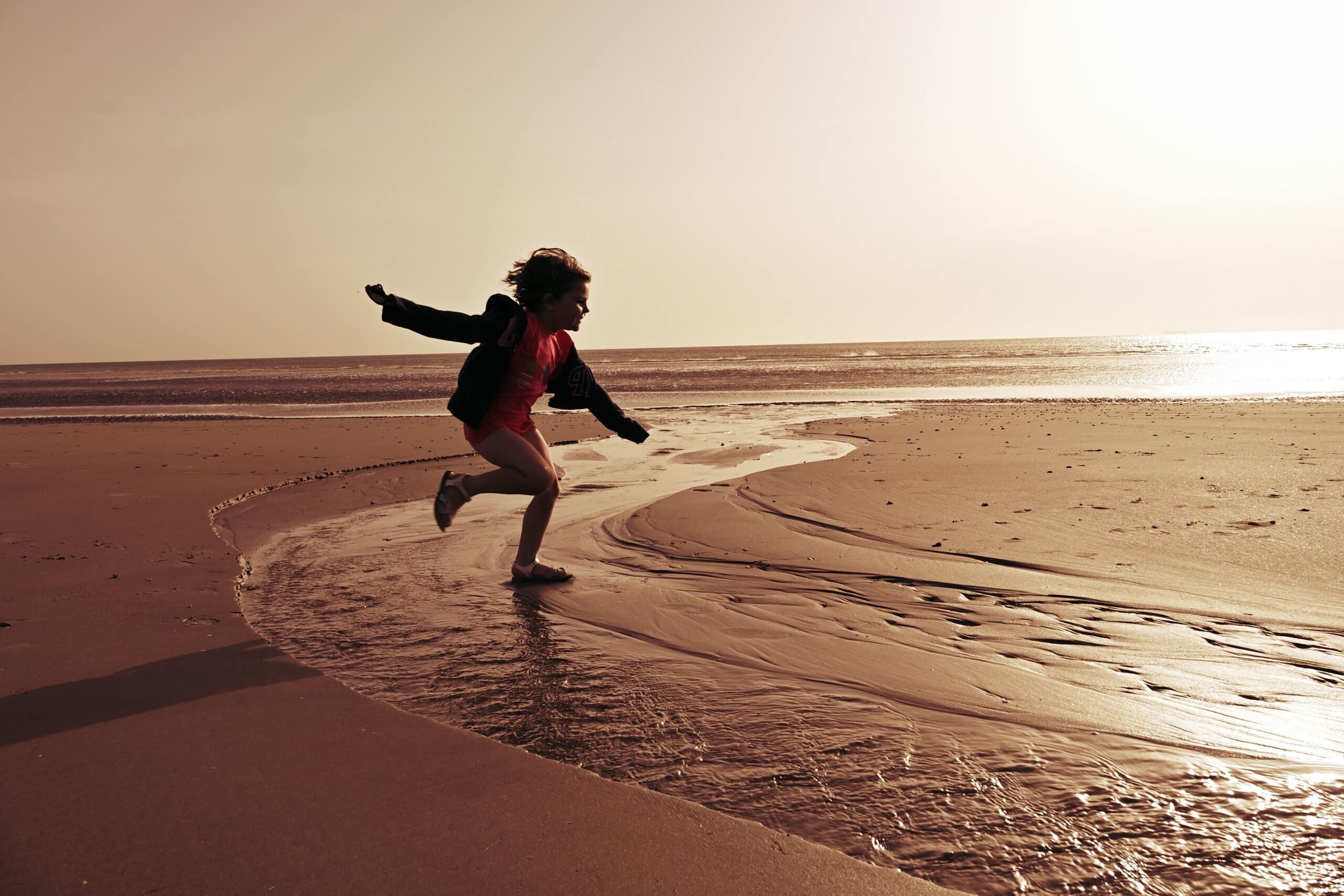 Fröhliches Kind läuft bei Sonnenuntergang an einem ruhigen Strand in Hauts-de-France, Frankreich.
