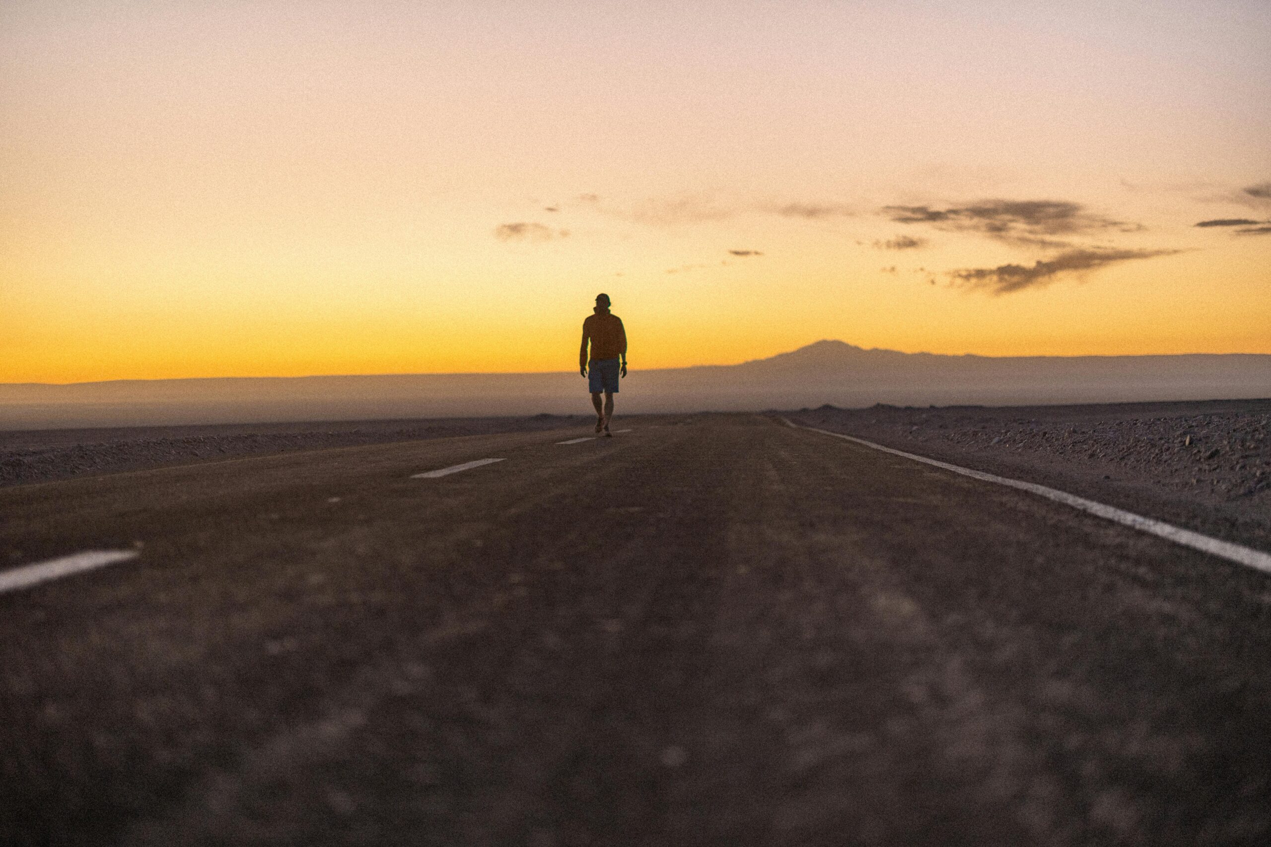 Eine einsame Gestalt geht bei Sonnenuntergang eine leere Straße in der riesigen Atacama-Wüste in Chile entlang.