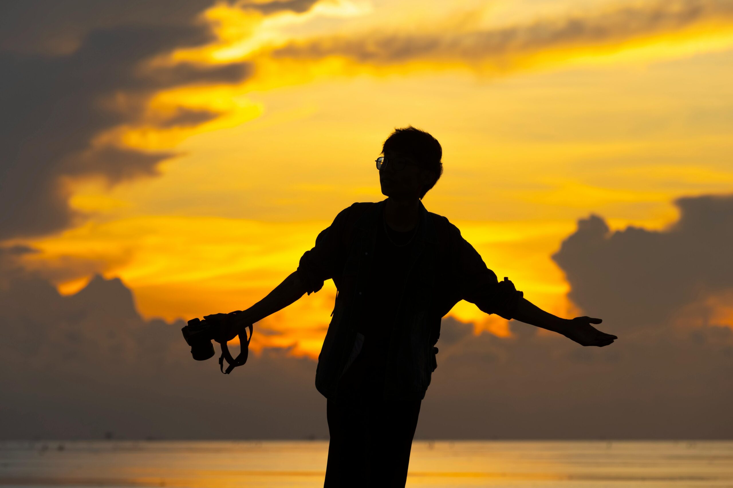 Silhouette einer Person, die eine Kamera vor einem dramatischen Sonnenuntergangshimmel hält.
