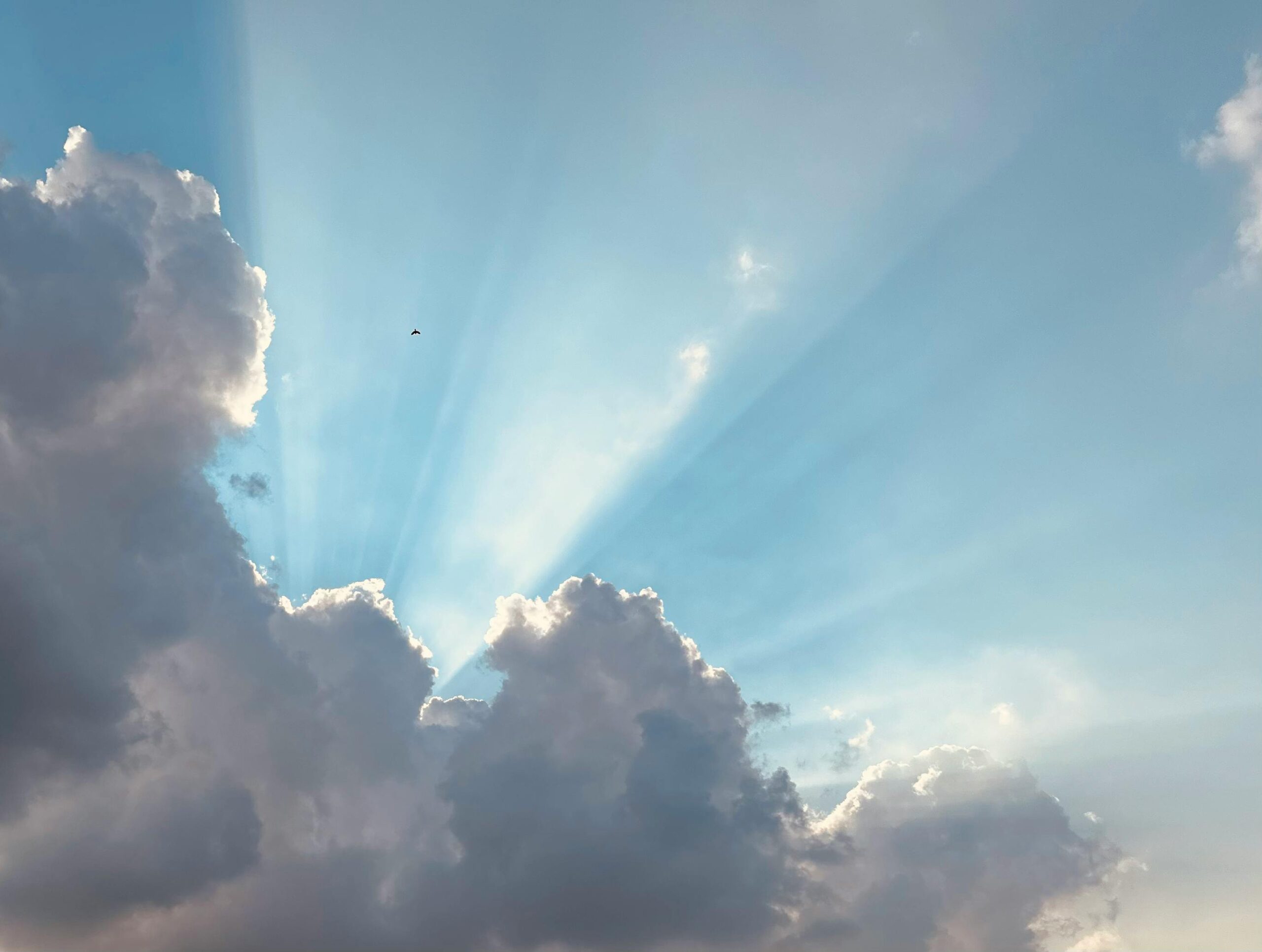 Atemberaubender Anblick von Sonnenstrahlen, die an einem klaren Tageshimmel durch flauschige Wolken brechen.