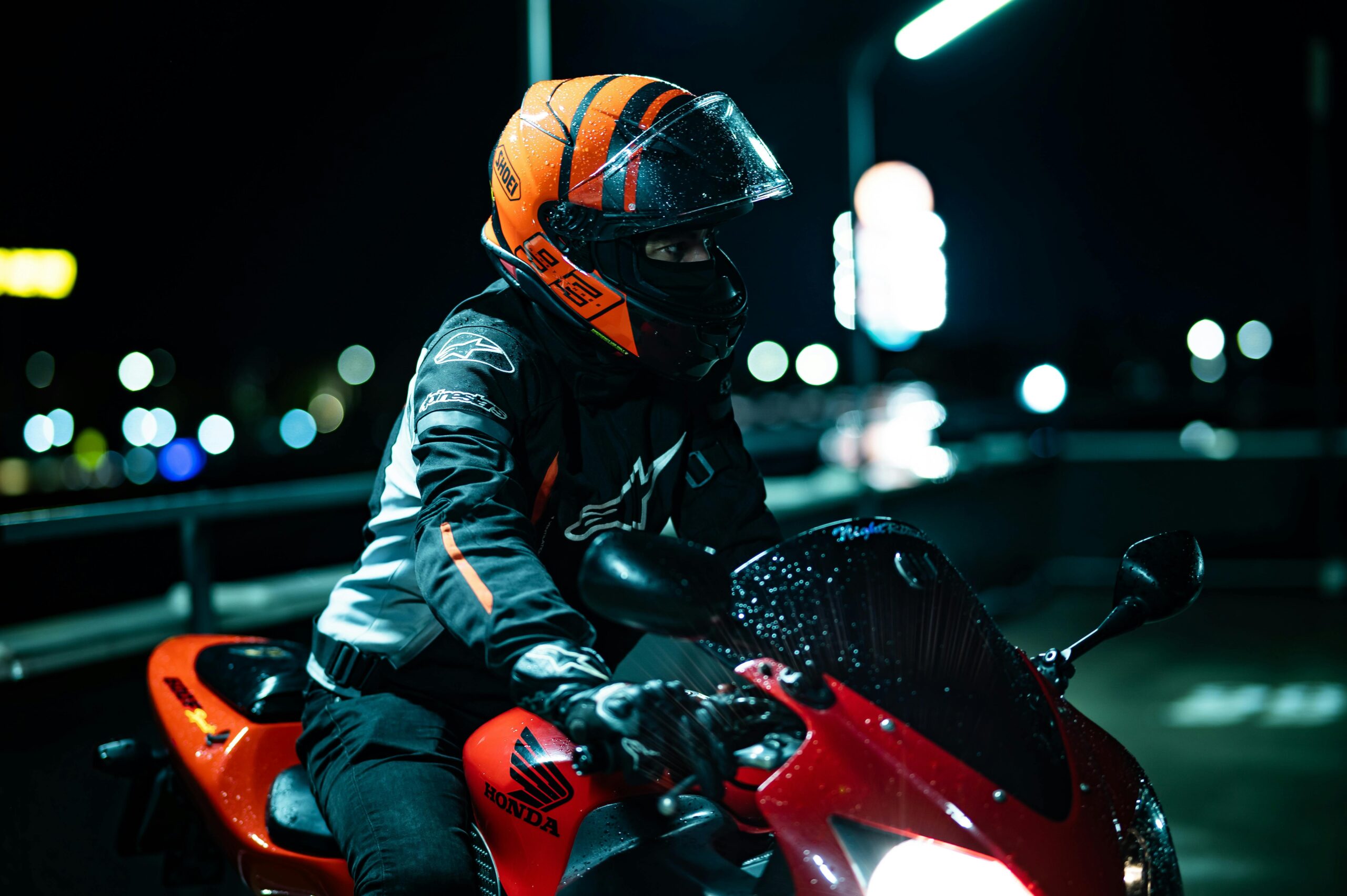 Ein Motorradfahrer in Schutzkleidung und mit orangefarbenem Helm fährt nachts ein rotes Motorrad.