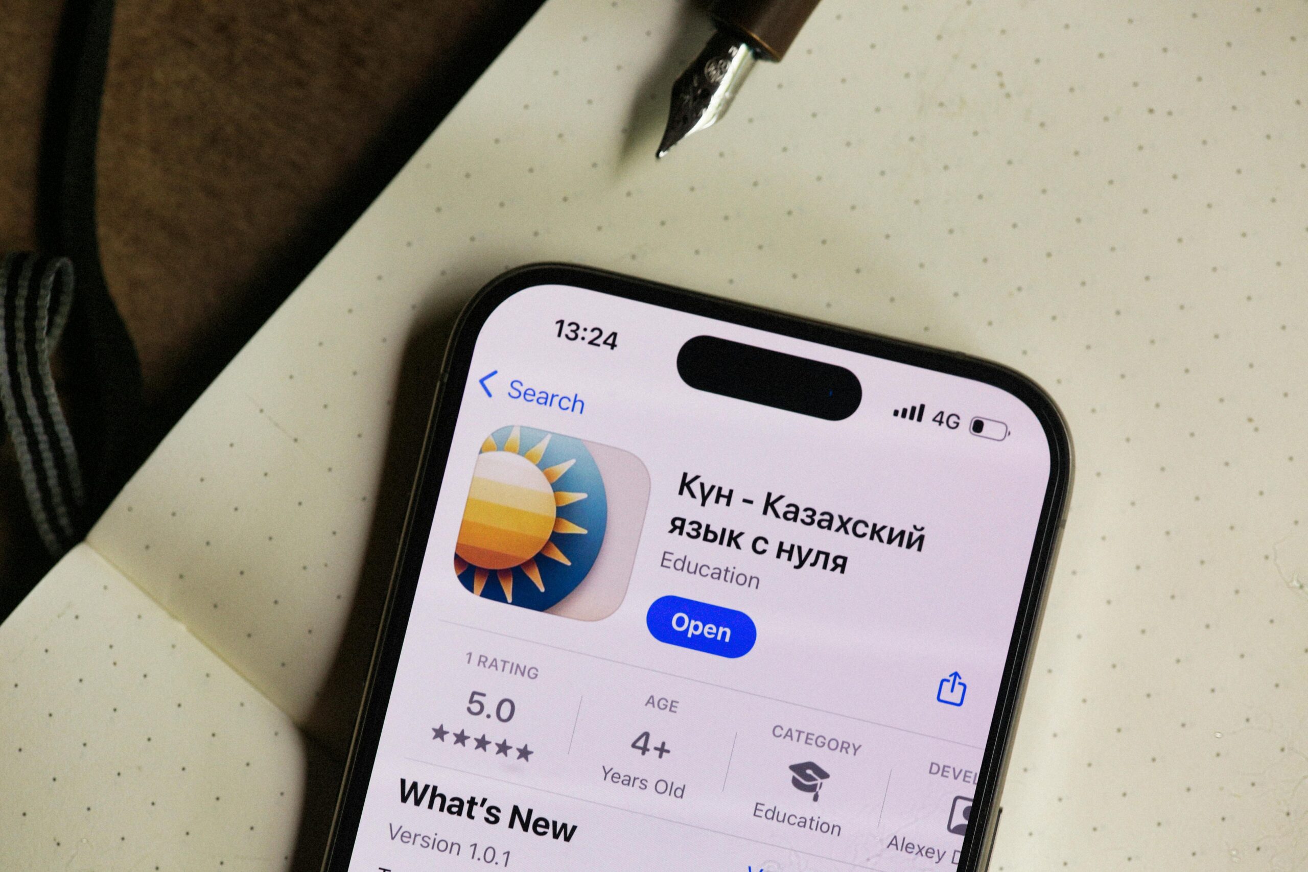 Nahaufnahme eines Smartphone-Bildschirms, der eine App zum Erlernen der kasachischen Sprache in einer geöffneten Notizbuchumgebung zeigt.