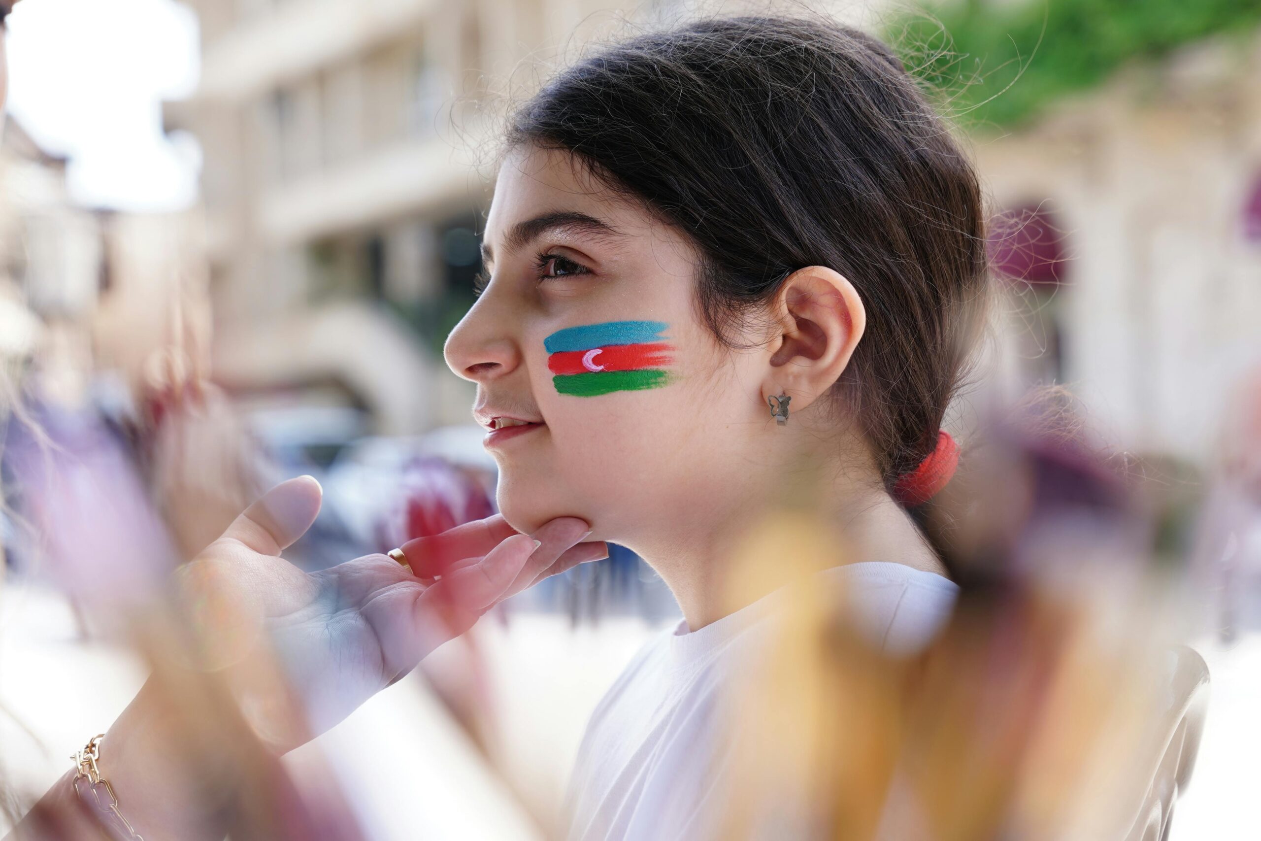Junges Mädchen mit auf die Wange gemalter aserbaidschanischer Flagge, im Freien.