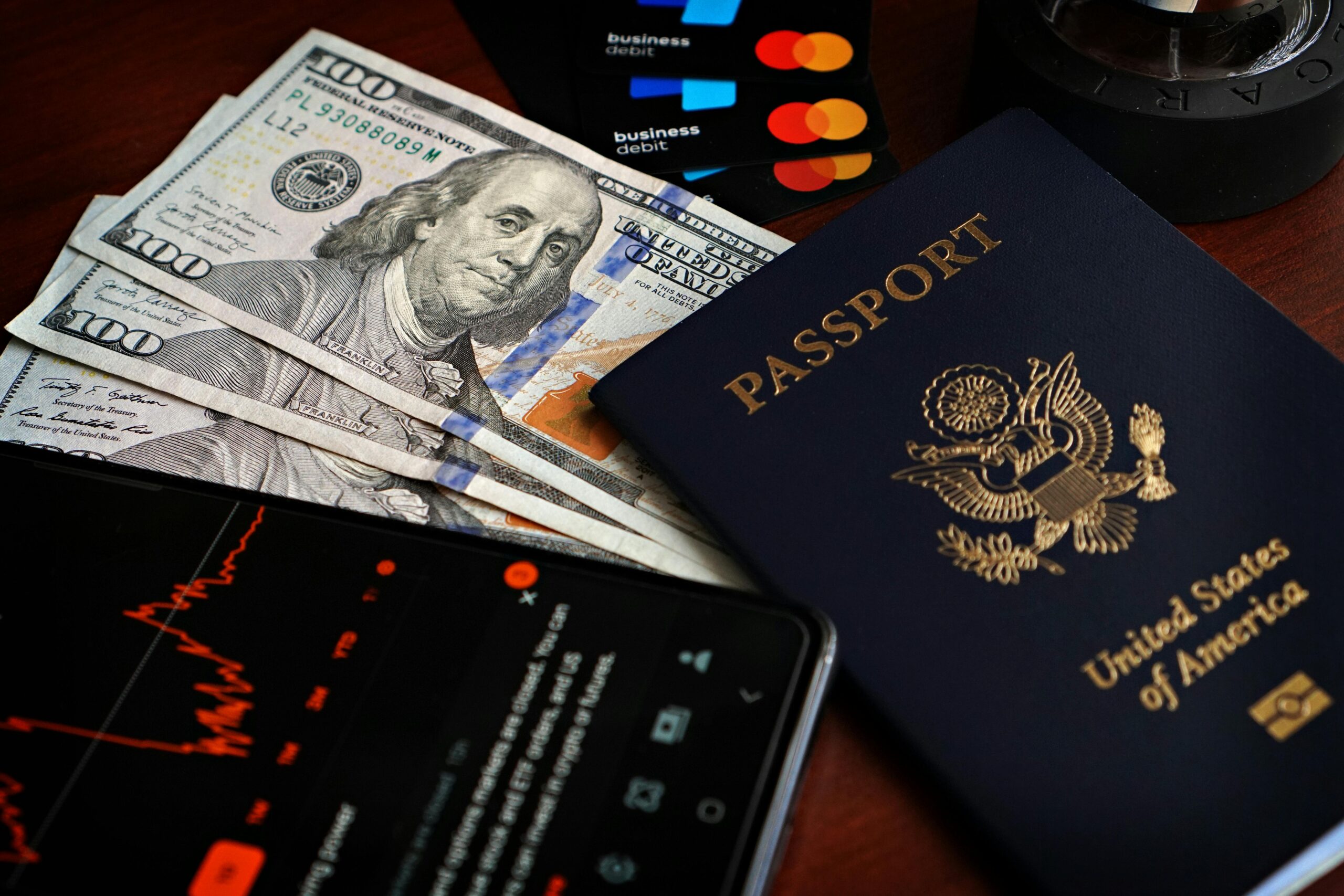 US-Reisepass mit Hundert-Dollar-Scheinen, Kreditkarten und Smartphone mit Aktiendaten.