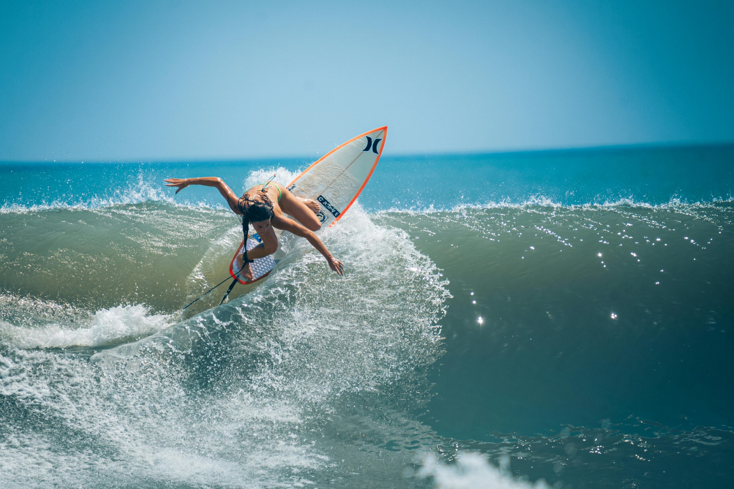 Aufregender Moment eines Surfers, der unter der strahlenden Sonne auf einer Welle reitet und dabei Geschick und Beweglichkeit demonstriert.