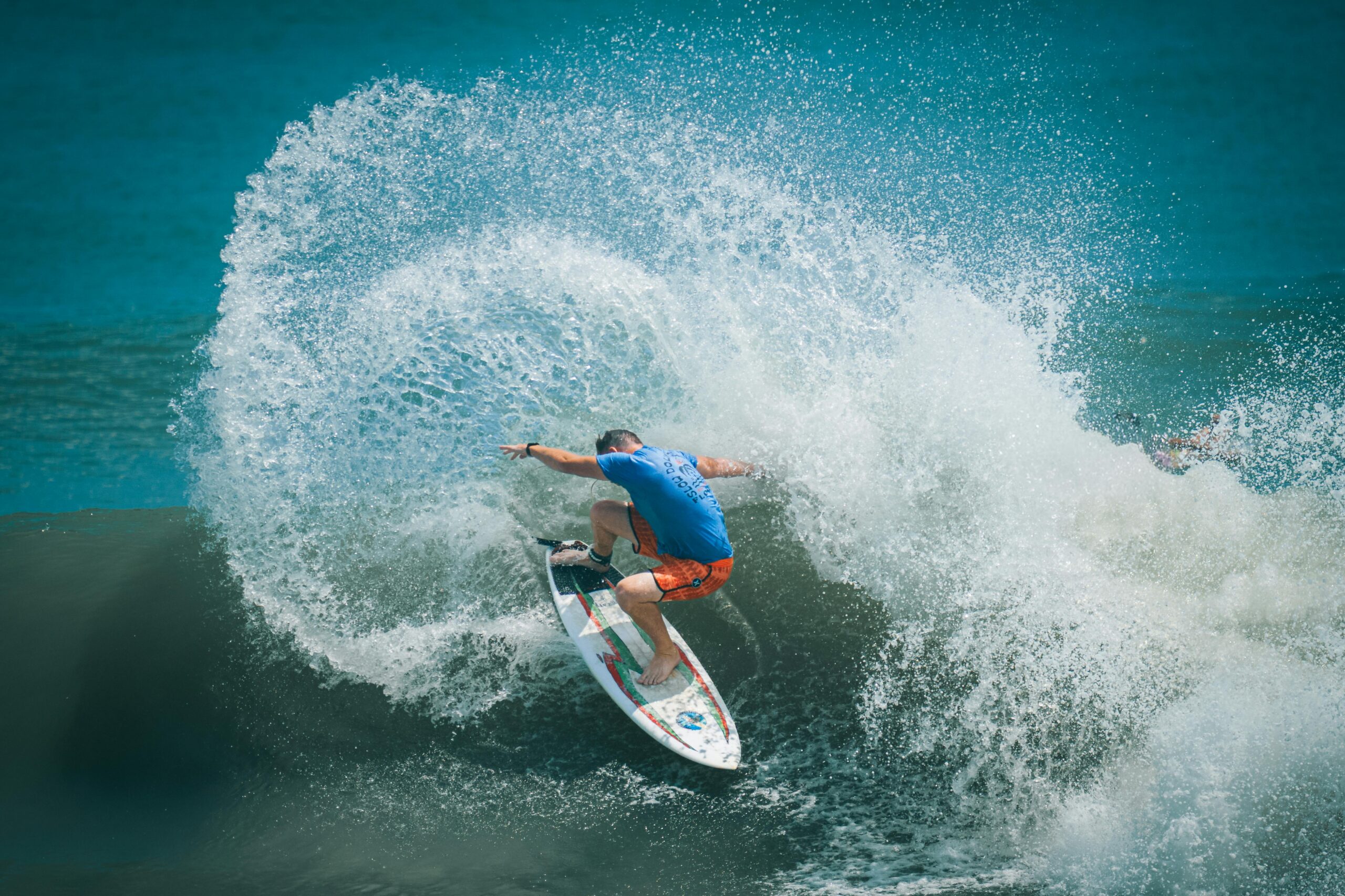 Aufregende Aufnahme eines Surfers in orangefarbenen Shorts, der durch eine kraftvolle Meereswelle gleitet.