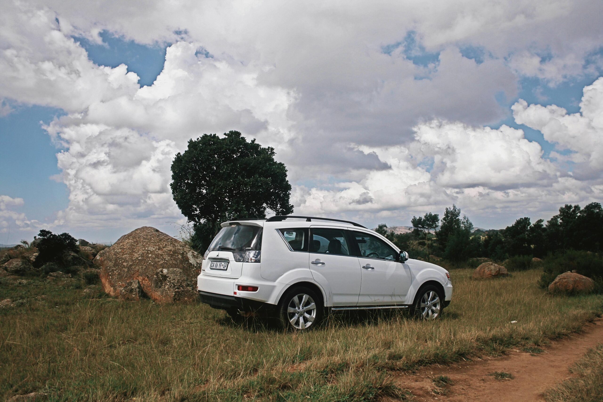 Ein weißer SUV parkt auf einer Wiese neben einem Feldweg unter einem strahlend bewölkten Himmel in Manzini, Eswatini.
