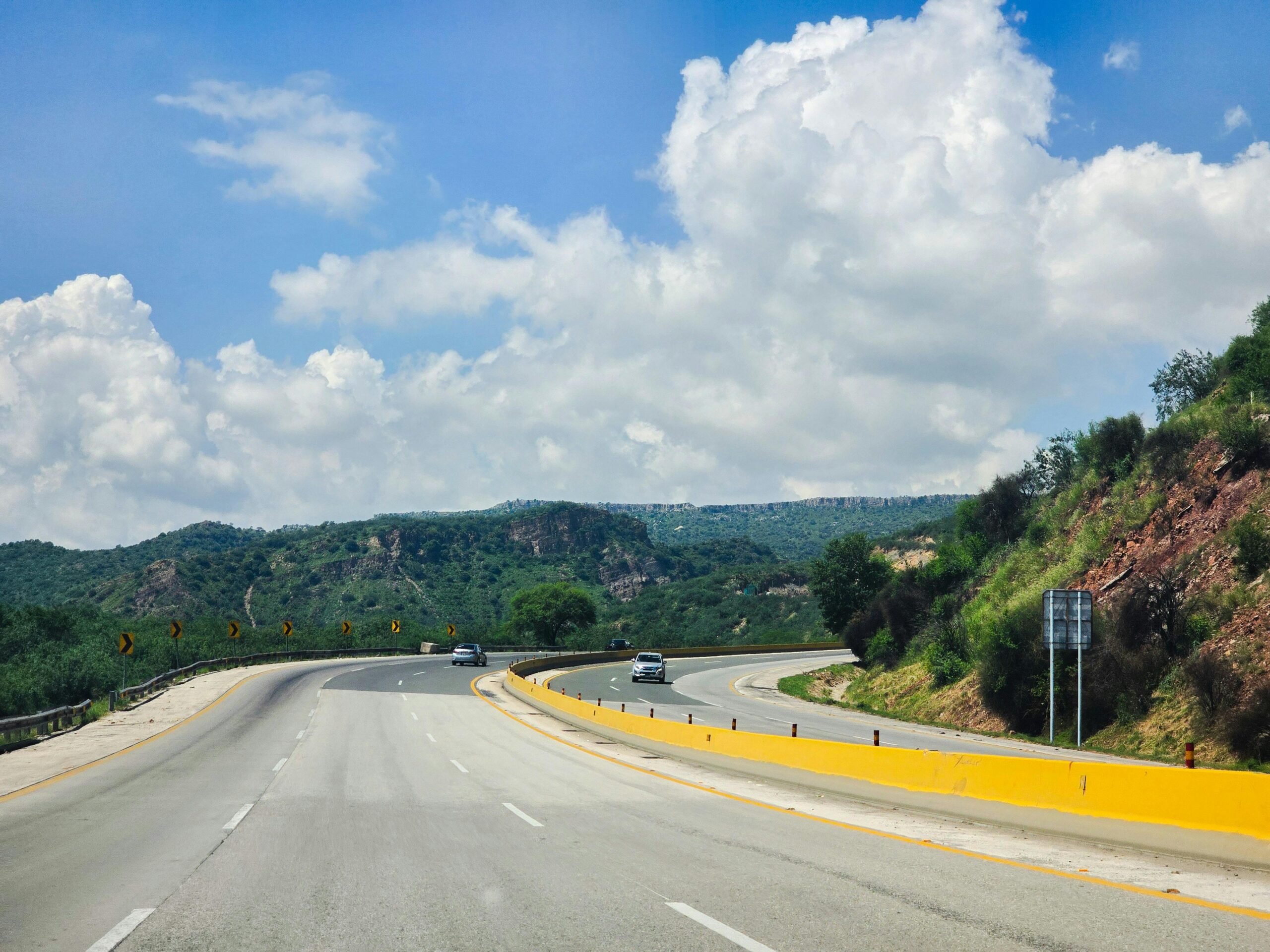 Eine malerische Autobahnkurve durch grüne Hügel unter einem strahlenden Himmel, ideal für Reise- und Naturthemen.
