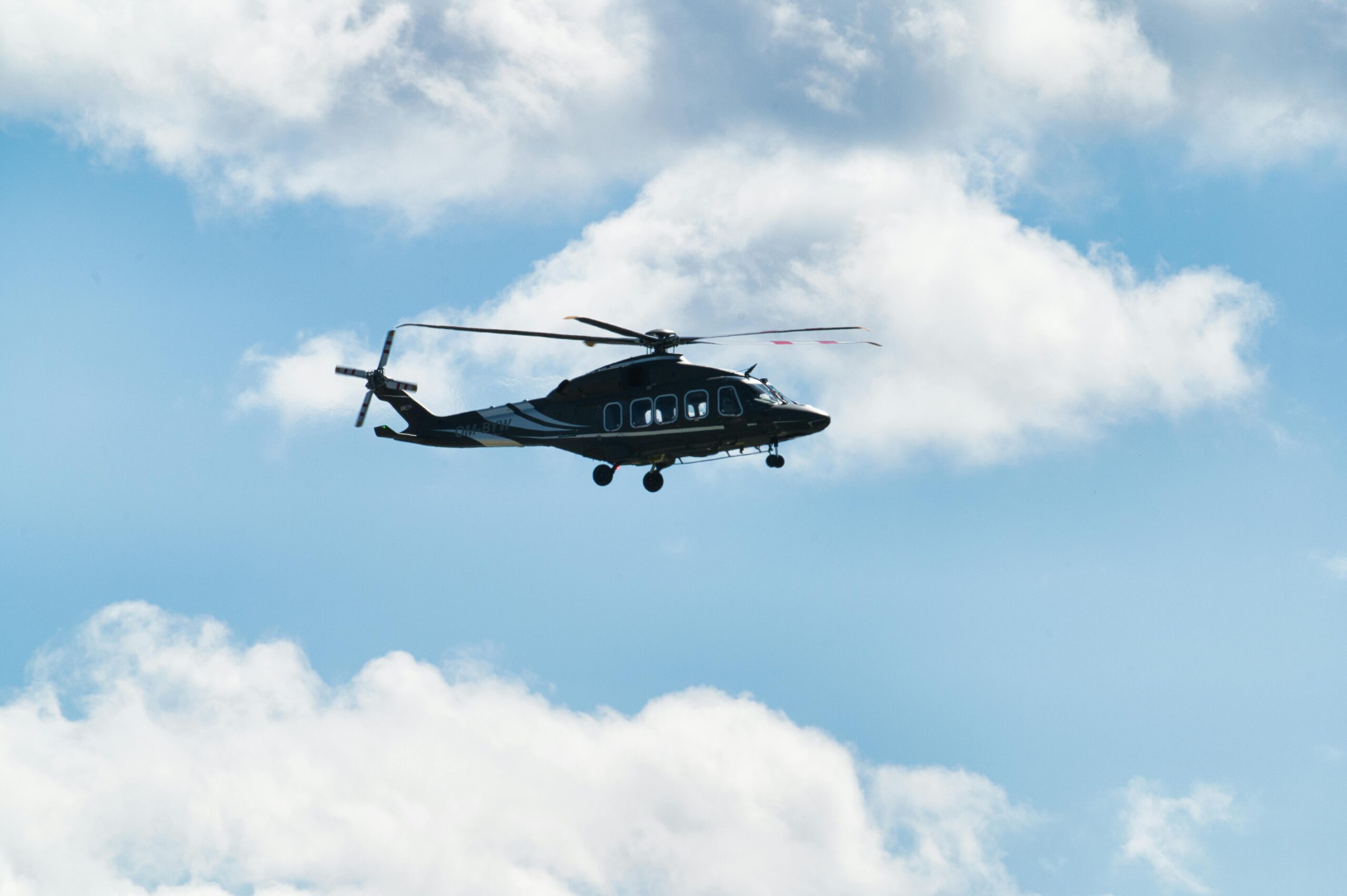 Ein eleganter Hubschrauber fliegt hoch vor einem strahlend blauen Himmel mit flauschigen Wolken, aufgenommen über Poprad, Slowakei.
