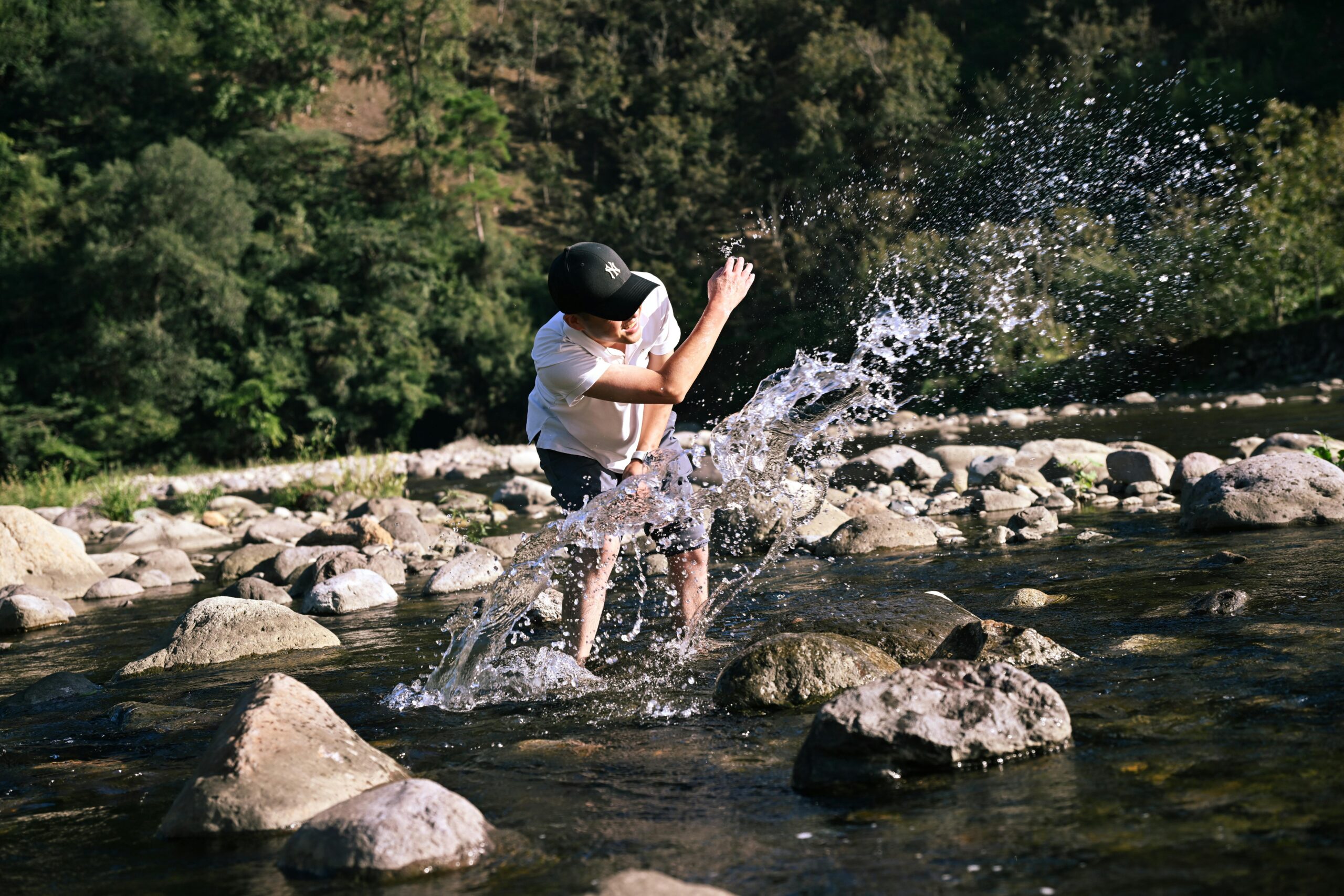 Ein Mann planscht in einer felsigen Flusslandschaft mit Wasser und fängt die Freude eines sonnigen Outdoor-Erlebnisses ein.