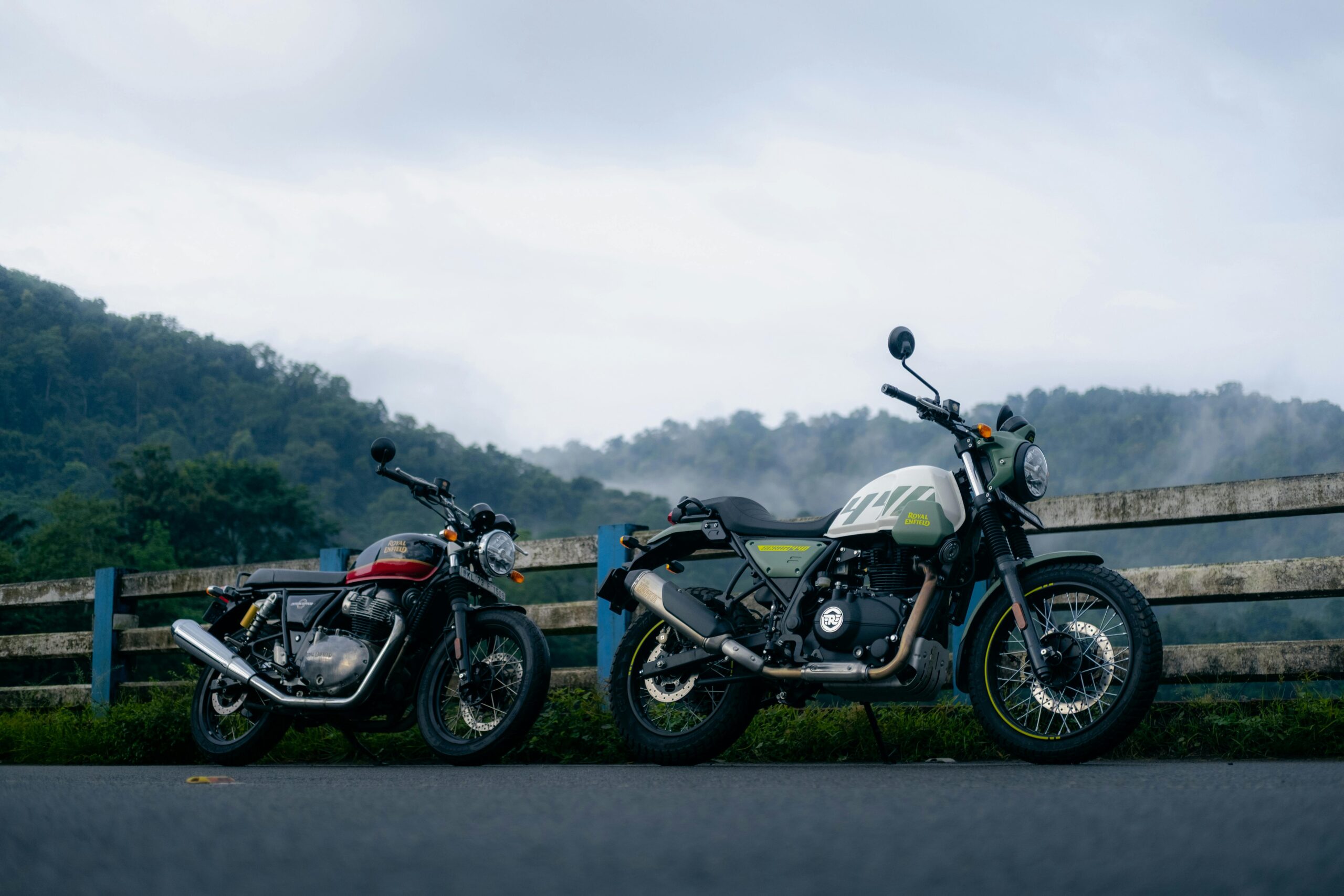 Zwei Oldtimer-Motorräder parken vor einer nebligen Bergkulisse in Pariyaram, Kerala.
