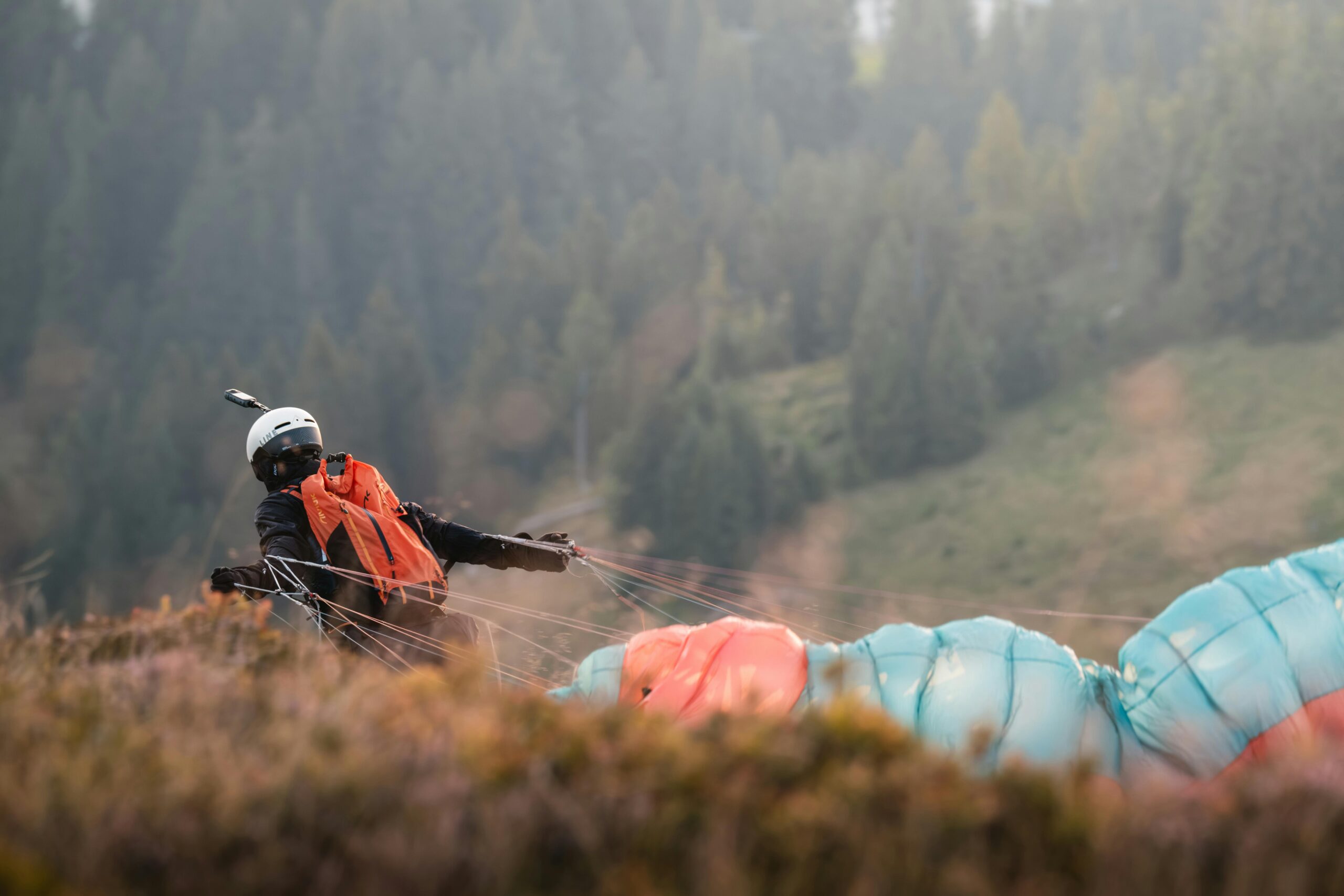 Ein Gleitschirm bereitet sich in einer bewaldeten Bergregion auf den Start vor und fängt Abenteuer und Spannung im Freien ein.