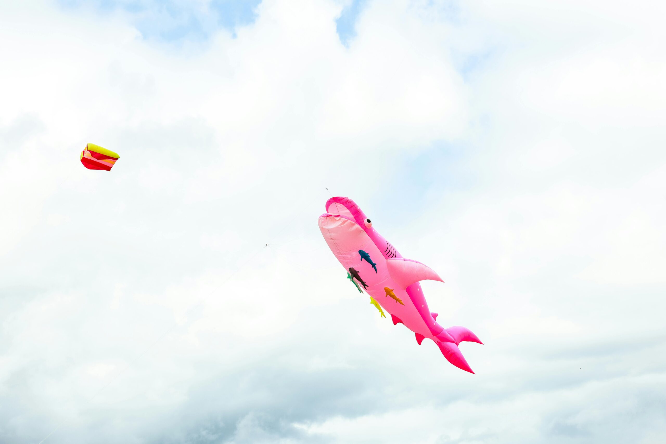 Ein leuchtend rosa Drachen in Haiform schwebt vor einem Wolkenhintergrund und ruft Freude und Freiheit hervor.
