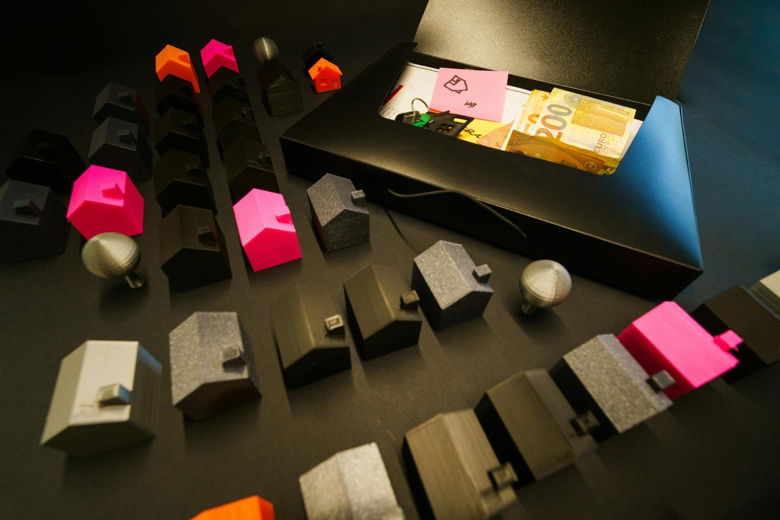Bunte Miniaturhäuser und Euro-Banknoten in einem Etui, die Immobilien und Finanzen repräsentieren.