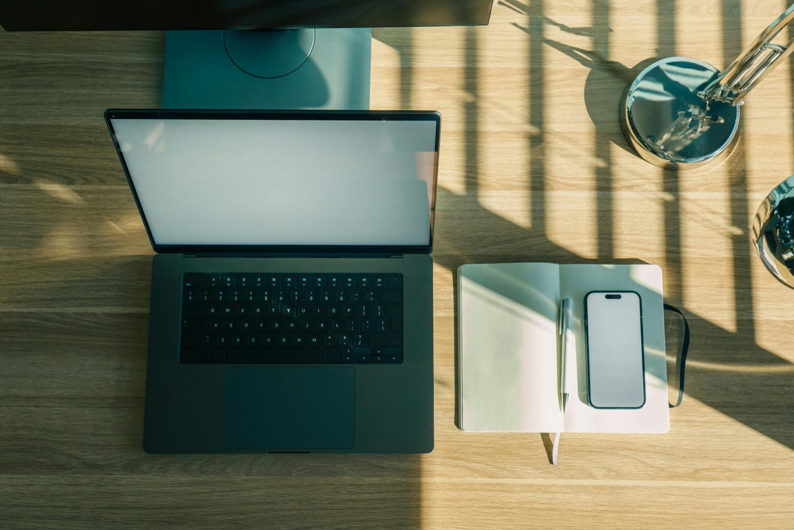 Ein sauberer und aufgeräumter Schreibtisch mit Laptop, Notizbuch, Stift und Smartphone bei natürlichem Licht.