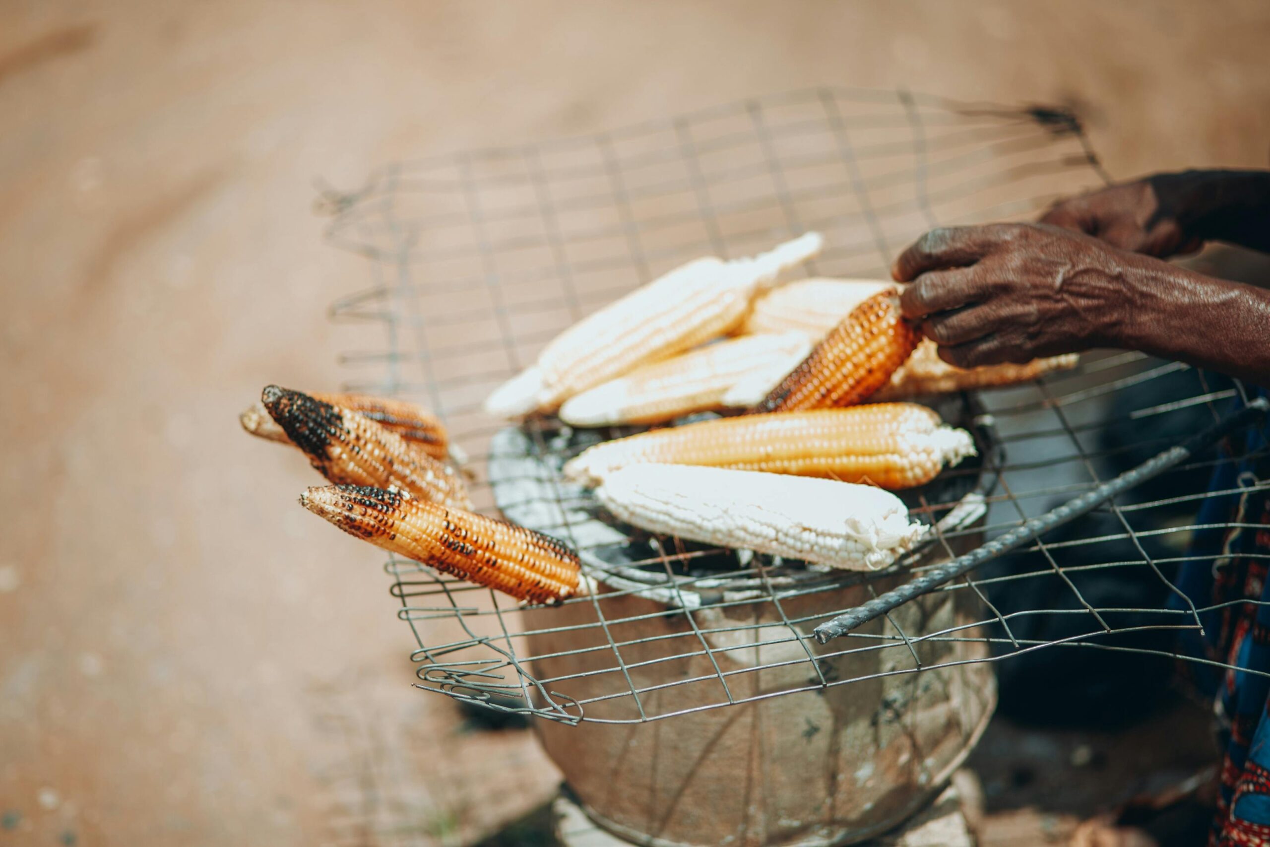 Eine ältere Frau röstet Mais über offenem Feuer in Kaduna, Nigeria, und demonstriert so traditionelle afrikanische Kochmethoden.