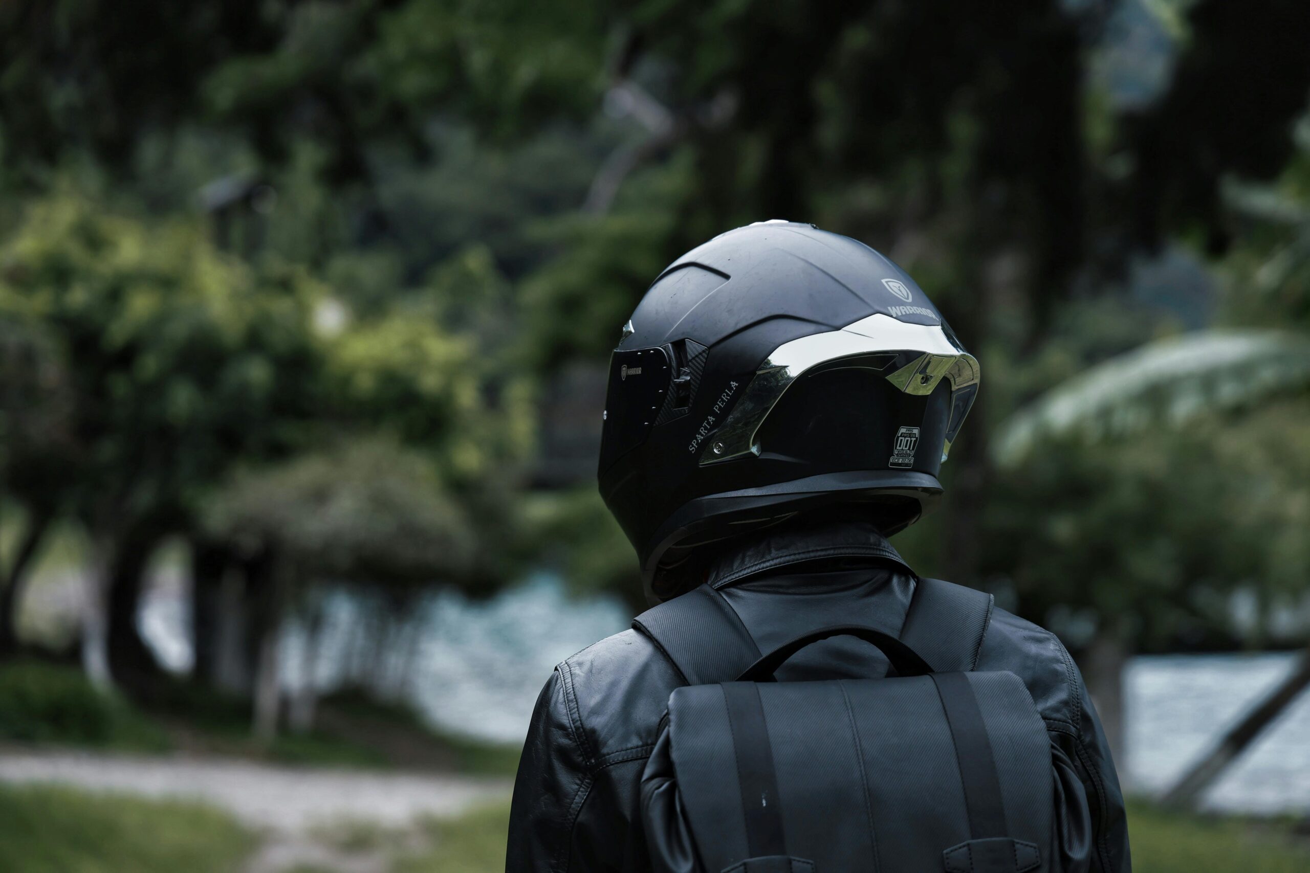 Rückansicht eines Motorradfahrers mit Helm und Rucksack in üppiger Natur.