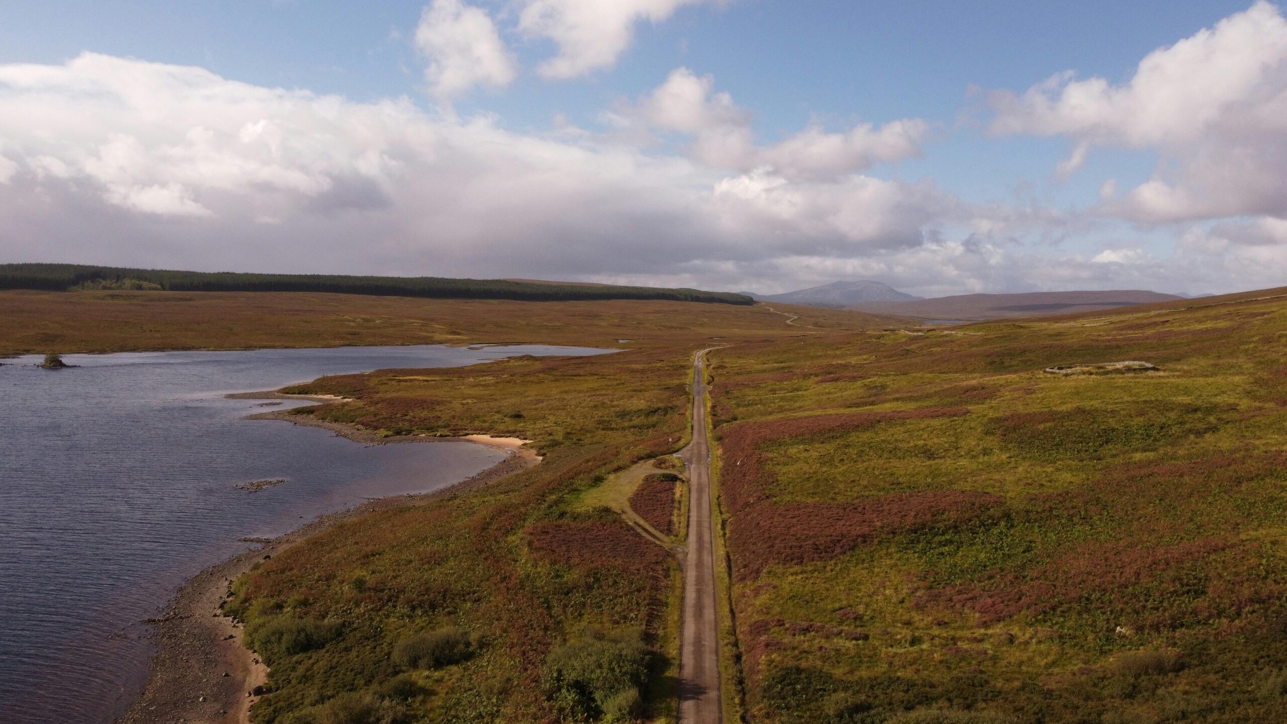 Luftaufnahme einer abgelegenen Straße an einem See in Schottland unter einem bewölkten Himmel.
