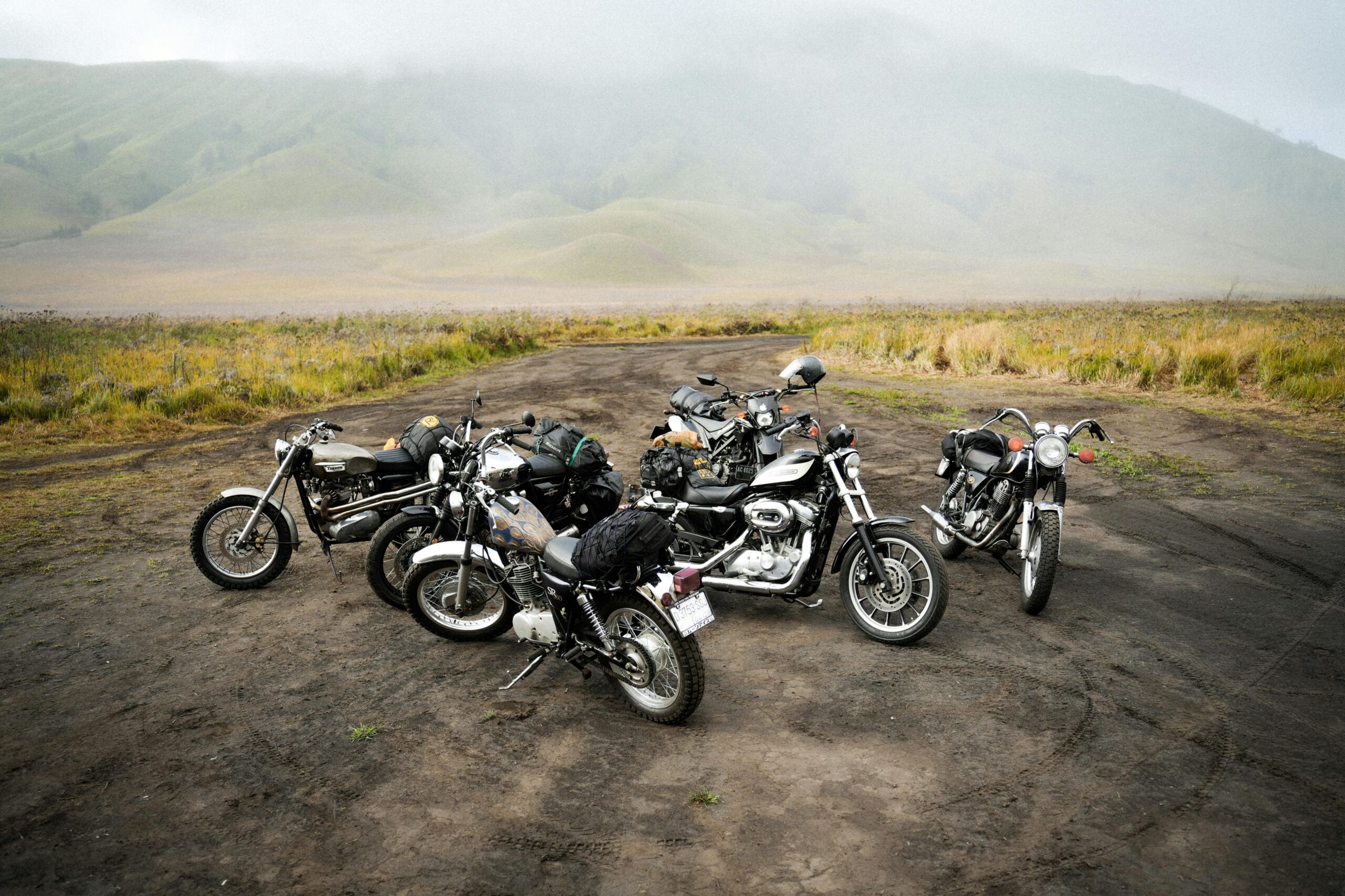 Fünf Motorräder, geparkt in einer nebligen, malerischen Landschaft, ideal für Abenteuer- und Reisethemen.