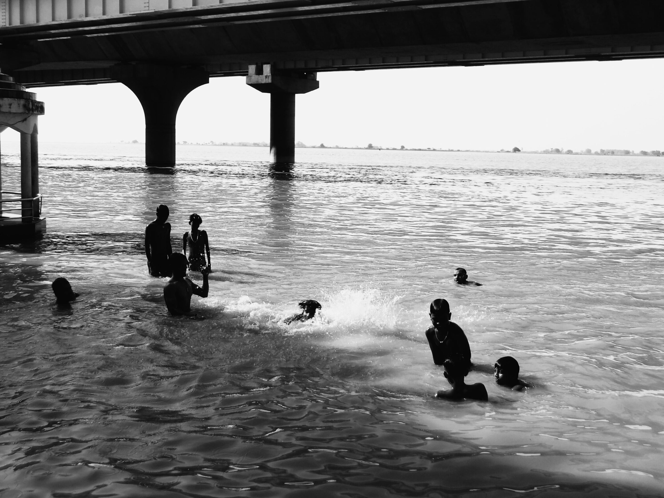 Ein Schwarzweißfoto von Kindern, die Spaß am Schwimmen unter einer Brücke haben.