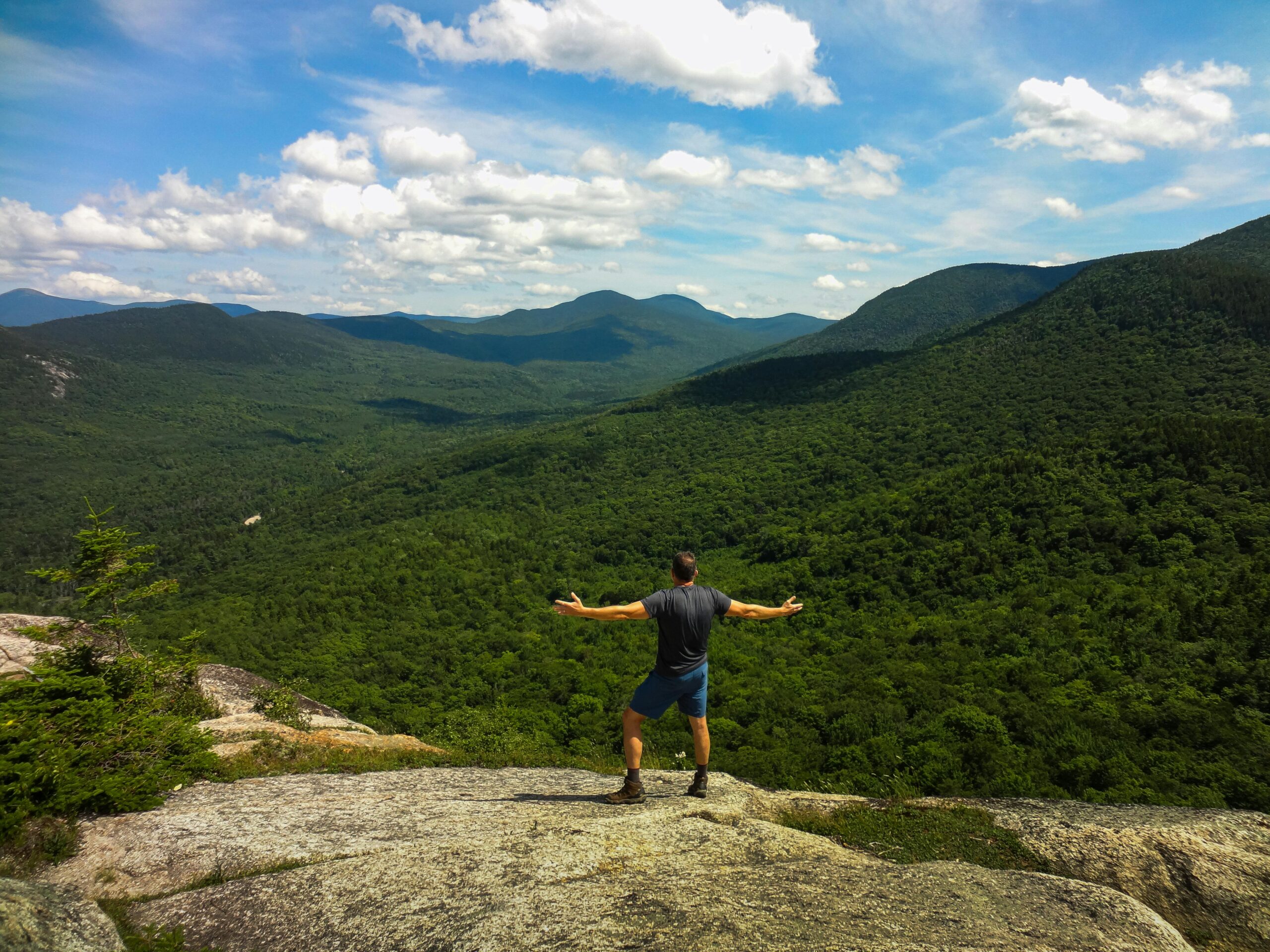 Wanderer genießt die Natur auf einer Felsklippe mit Blick auf üppige Täler in den White Mountains, NH.