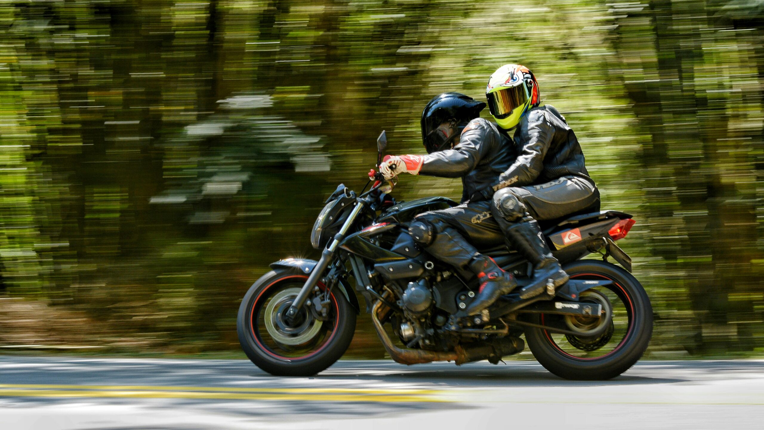 Zwei Motorradfahrer rasen über eine Waldstraße und vermitteln ein Gefühl von Nervenkitzel und Abenteuer.